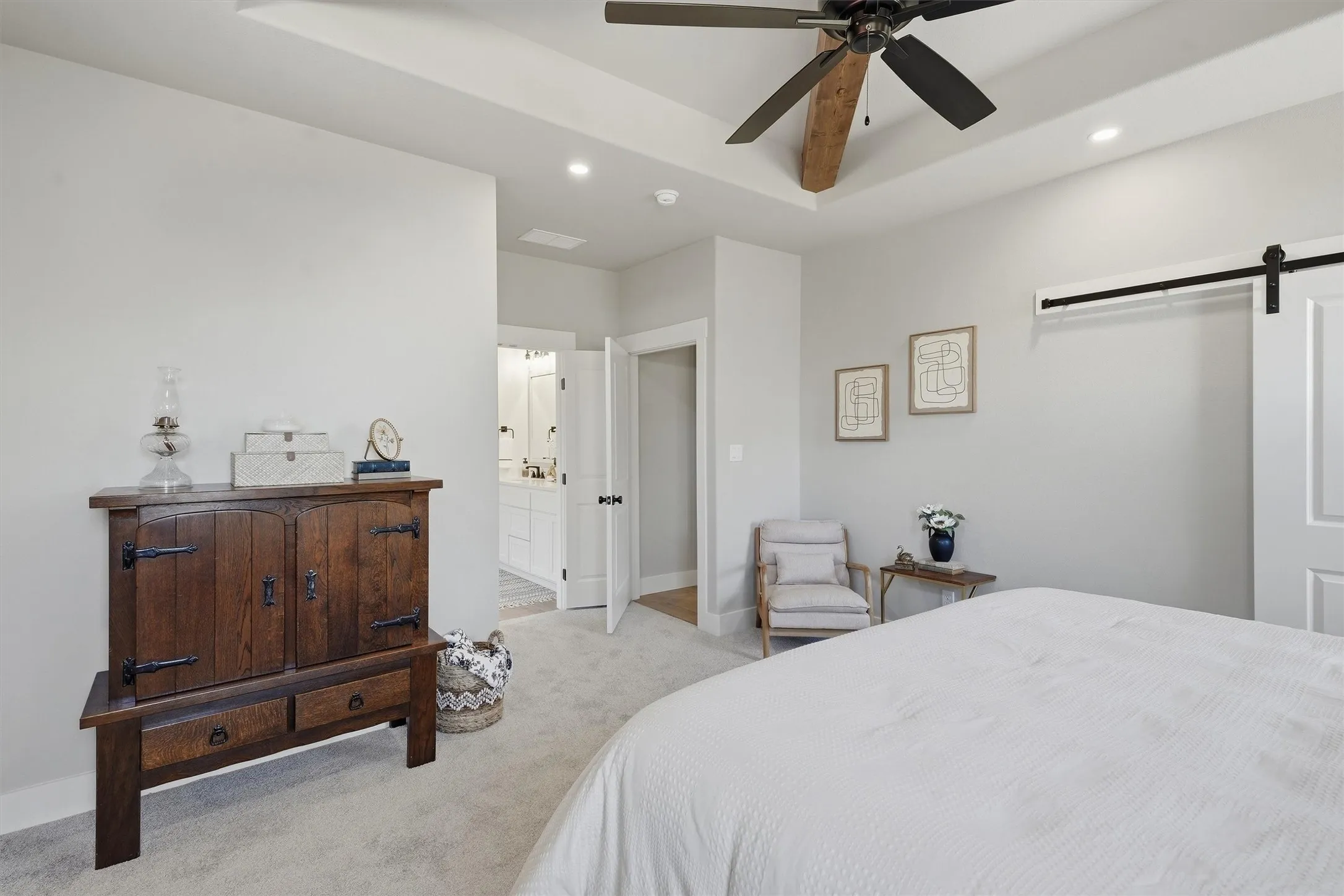 Tray ceiling with exposed wood beam, recessed lighting, ceiling fan, and barn door entry