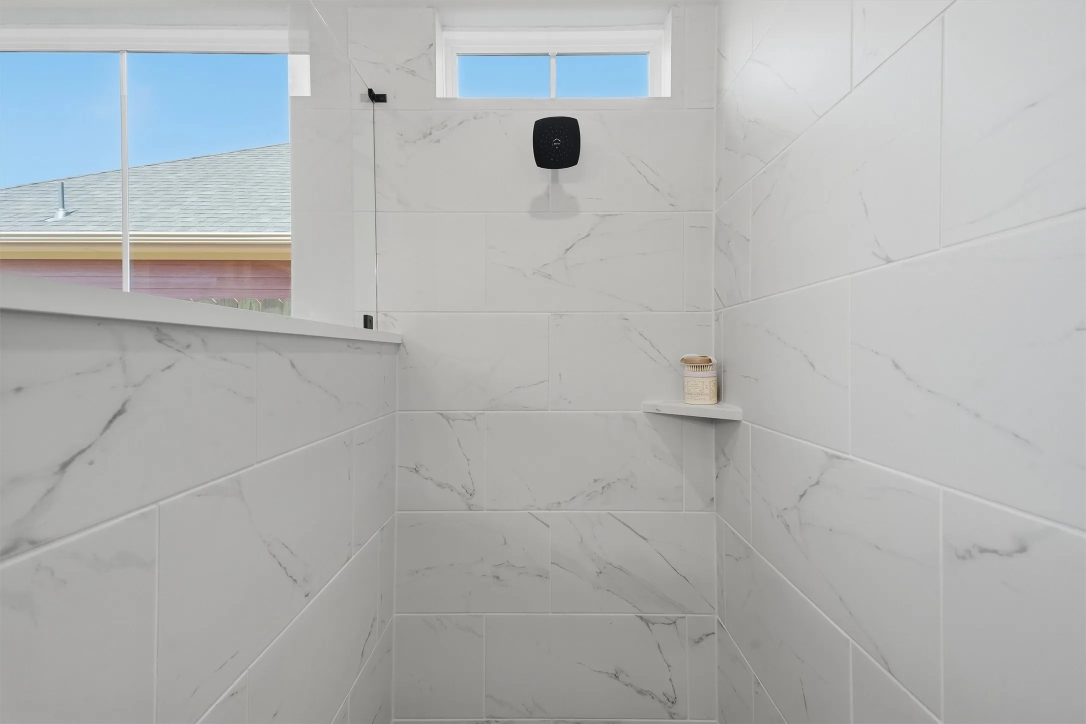 Shower enclosure featuring large format tile with subtle veining, a built-in corner shelf, and an overhead shower fixture