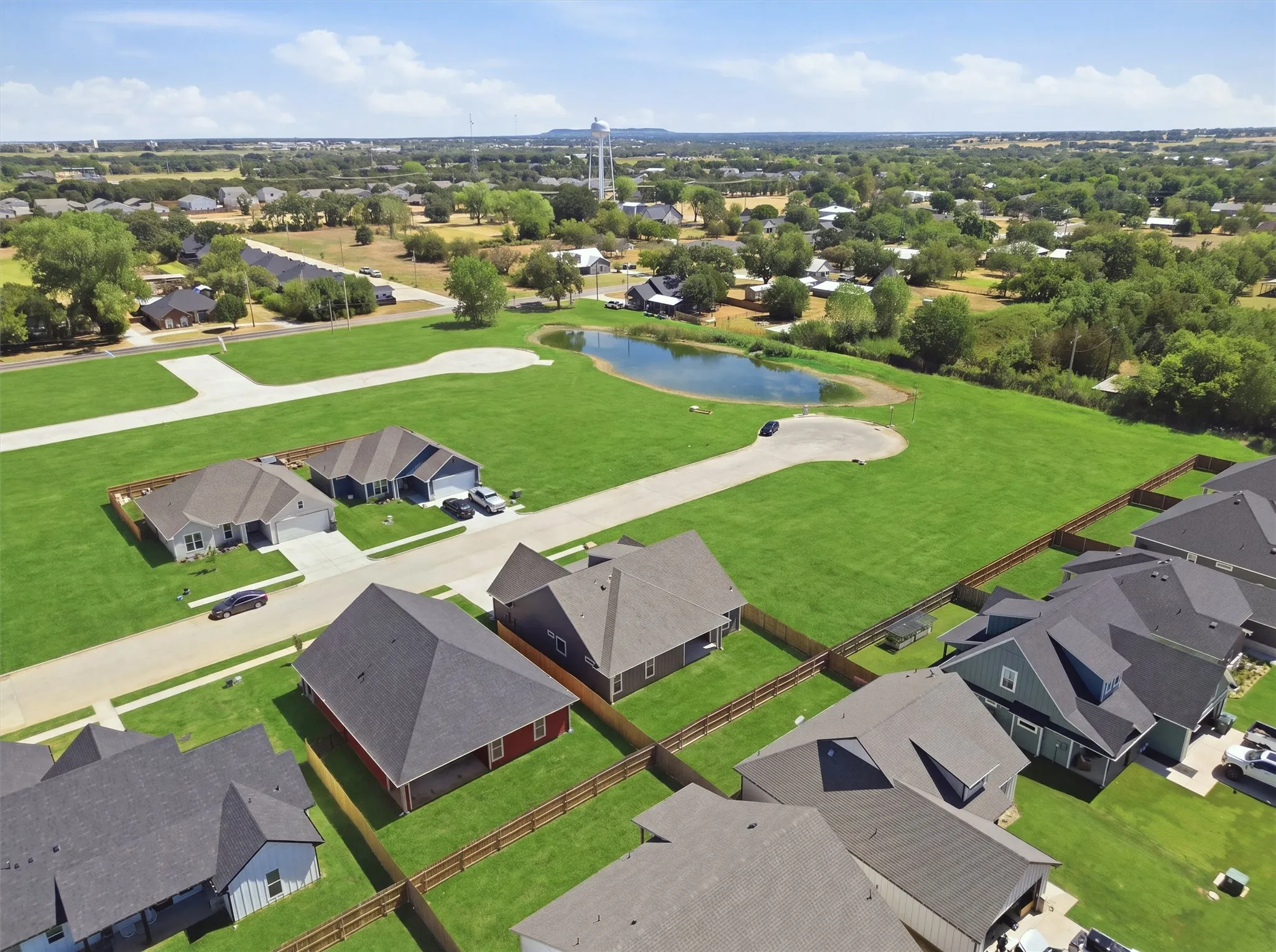 Expansive green spaces featuring a serene pond, paved streets, and new construction homes