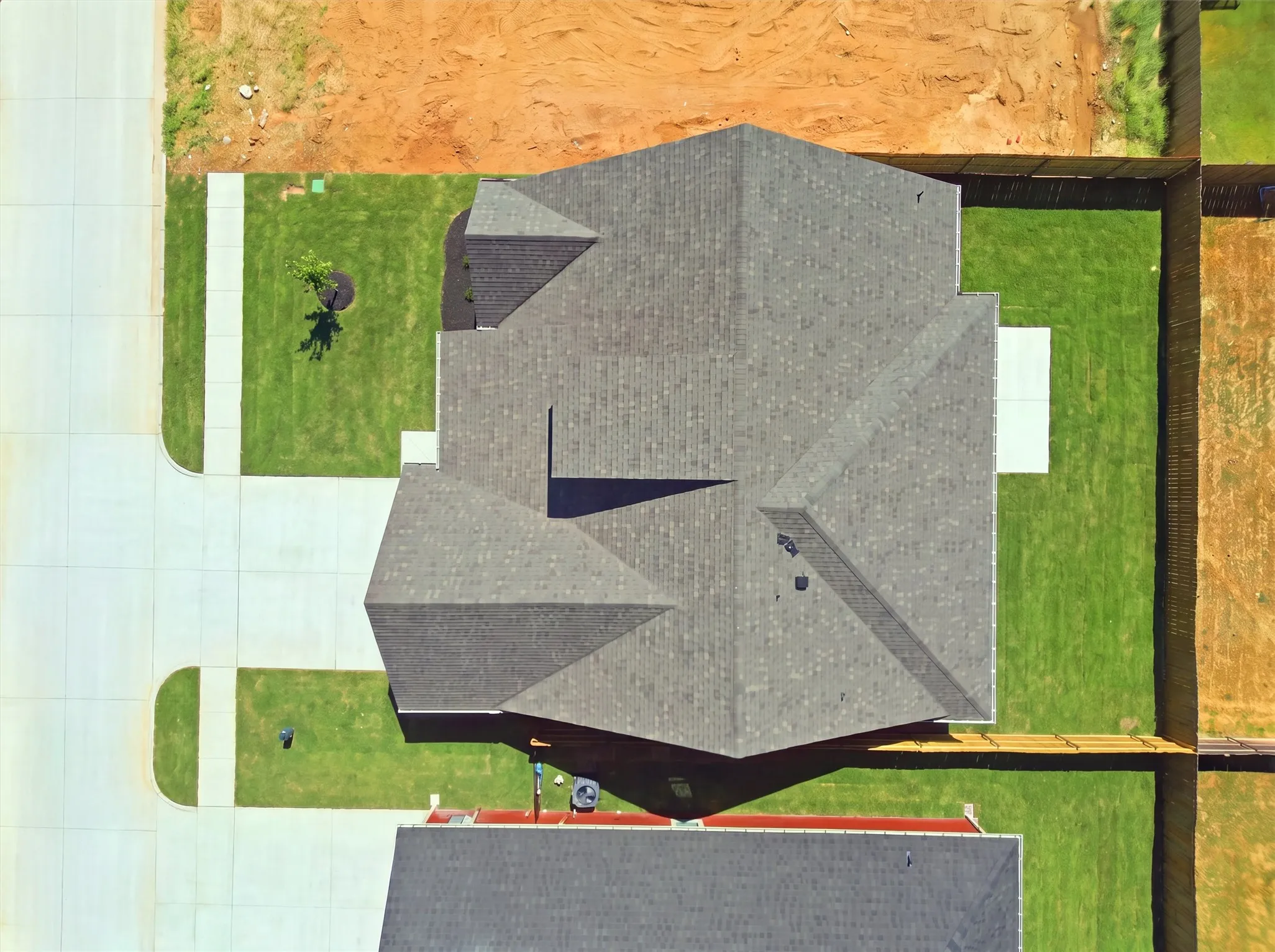 Pitched roof with dark shingles, concrete driveway, manicured lawn, and wood fencing