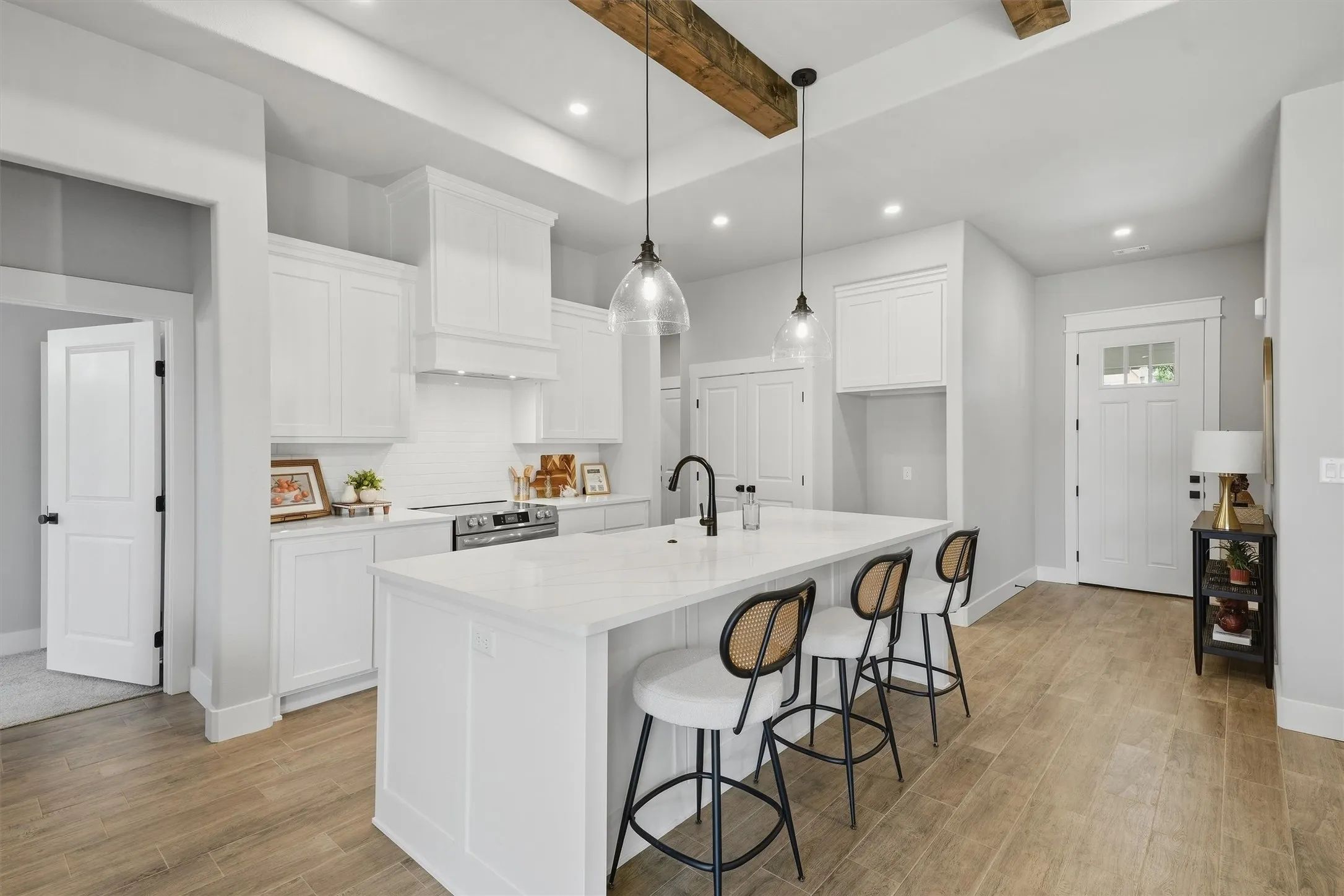 Bright kitchen with white cabinetry, wood-finish flooring, a central island with countertop, an integrated range, and exposed ceiling beams