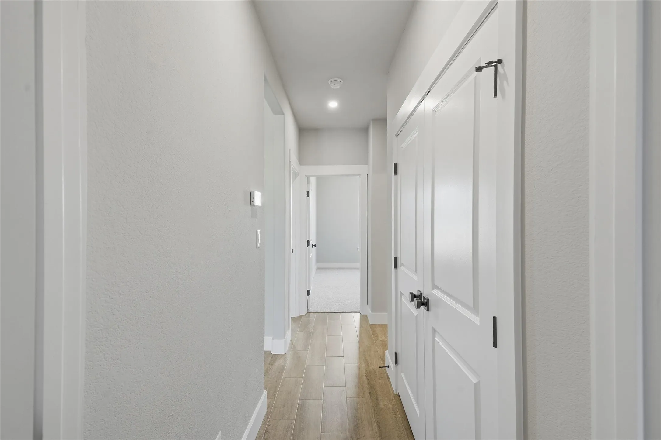 Hallway featuring wood-finish flooring, white paneled doors with matte black hardware, and recessed lighting