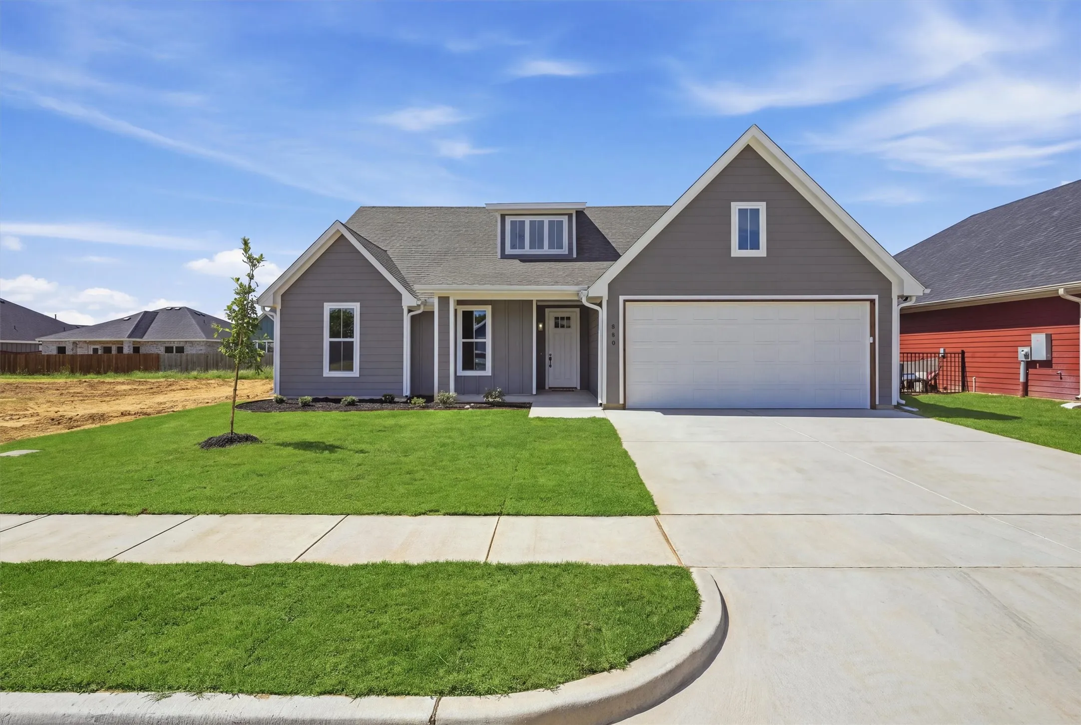 Gray siding exterior with white trim details, dormer window, attached garage, concrete driveway, and a verdant lawn