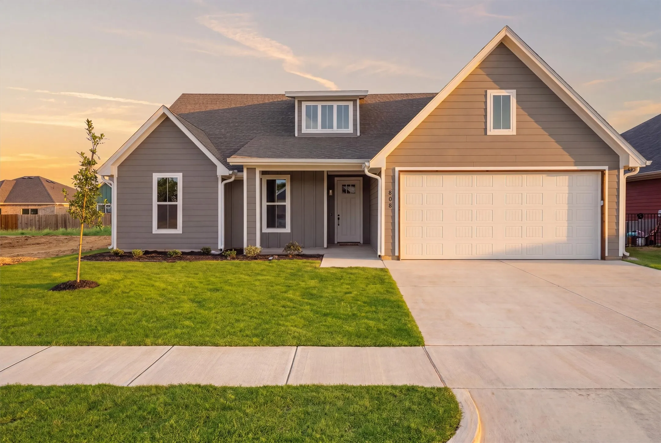 Contemporary exterior with gray siding, white trim, attached garage, concrete driveway, and a front lawn