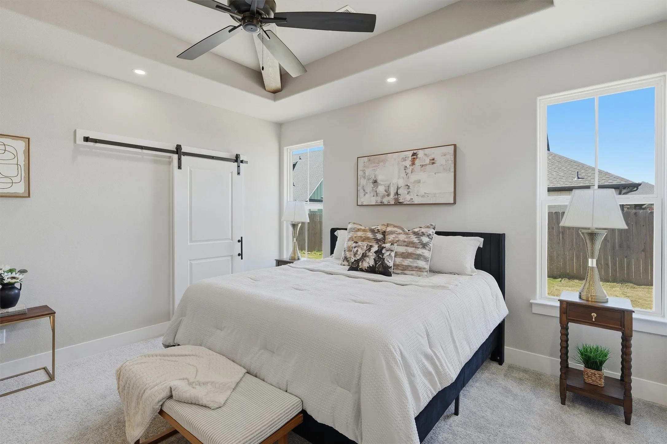 Tray ceiling with recessed lighting and a ceiling fan, white barn door, and a single window with a backyard outlook