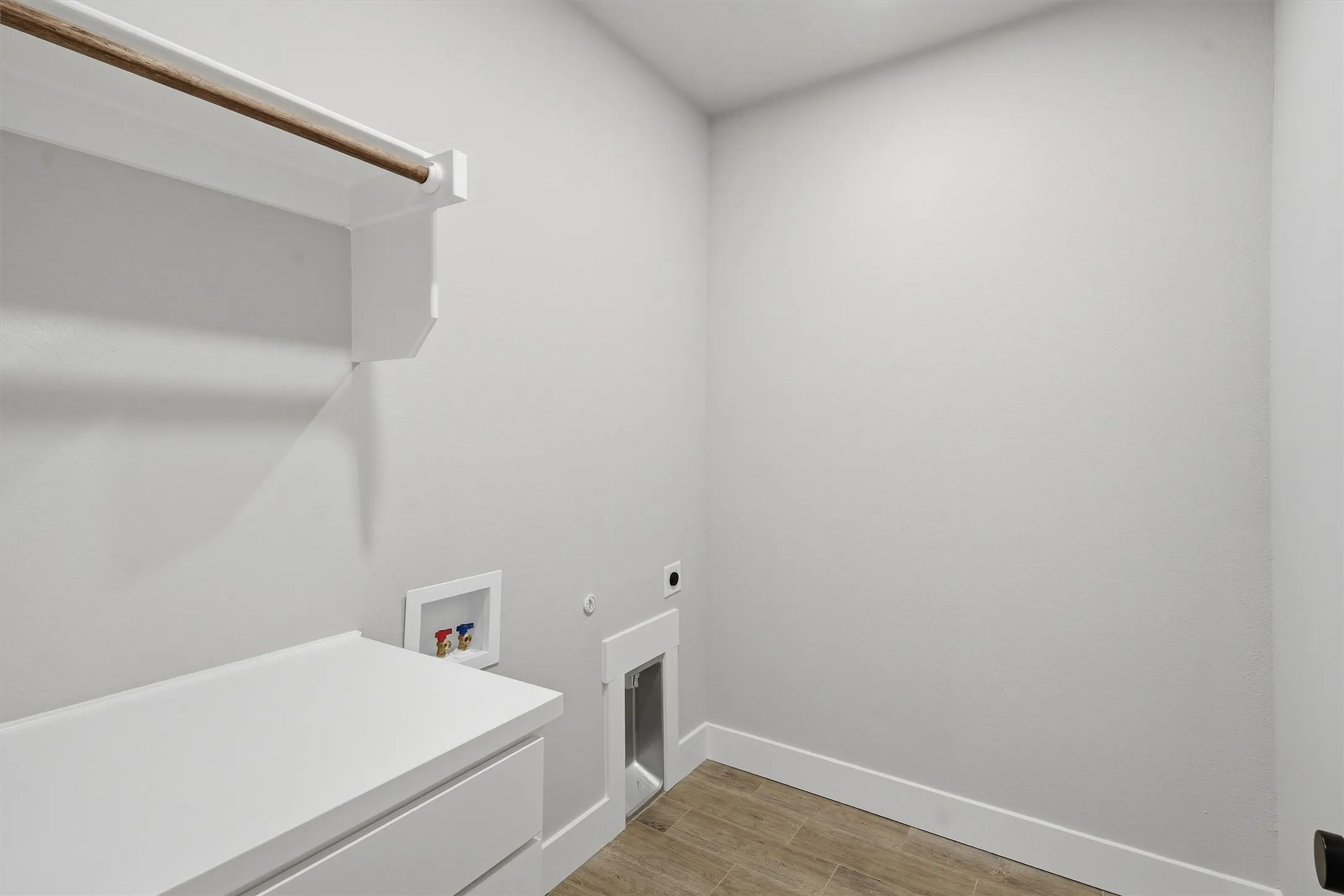 Built-in white cabinetry, integrated hanging rod, wood-finish flooring, and utility hookups