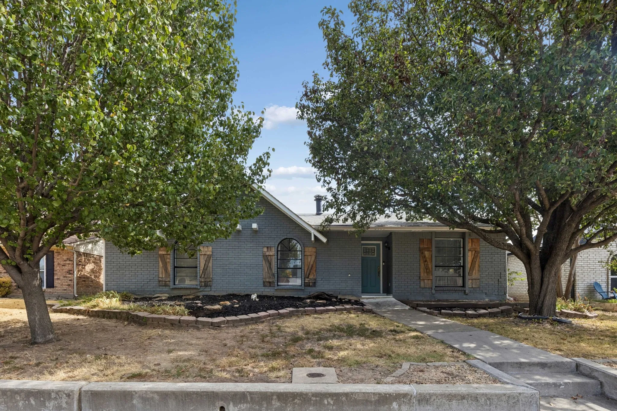 Welcoming Single-Story Profile - A wider view highlights the home’s approachable single-level design, established trees, and walkway leading directly to the sheltered front entrance.