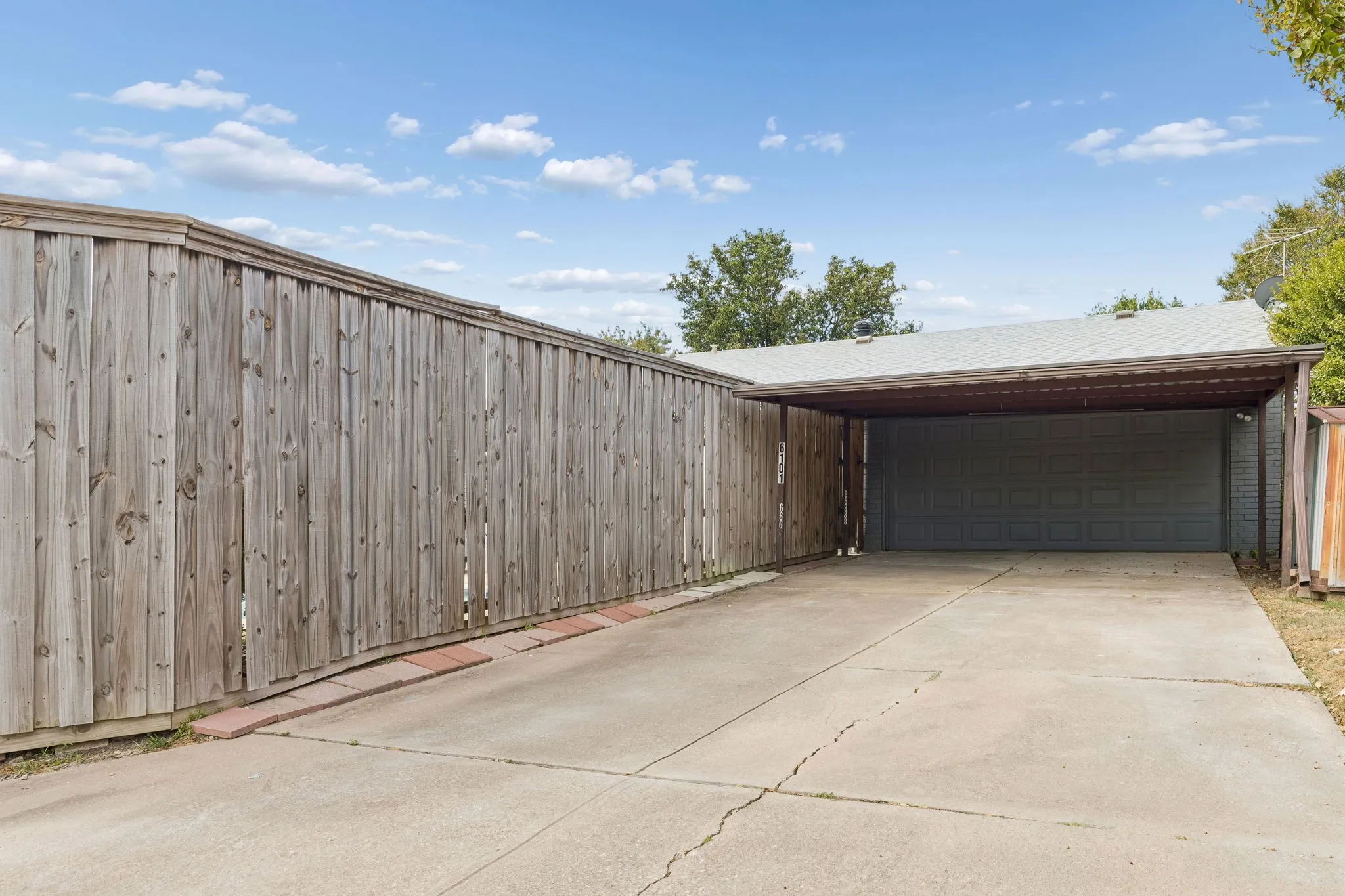 Generous Rear Parking - A wide driveway leads to the 2-car carport, offering convenient covered parking while the tall cedar privacy fence helps define the backyard setting.