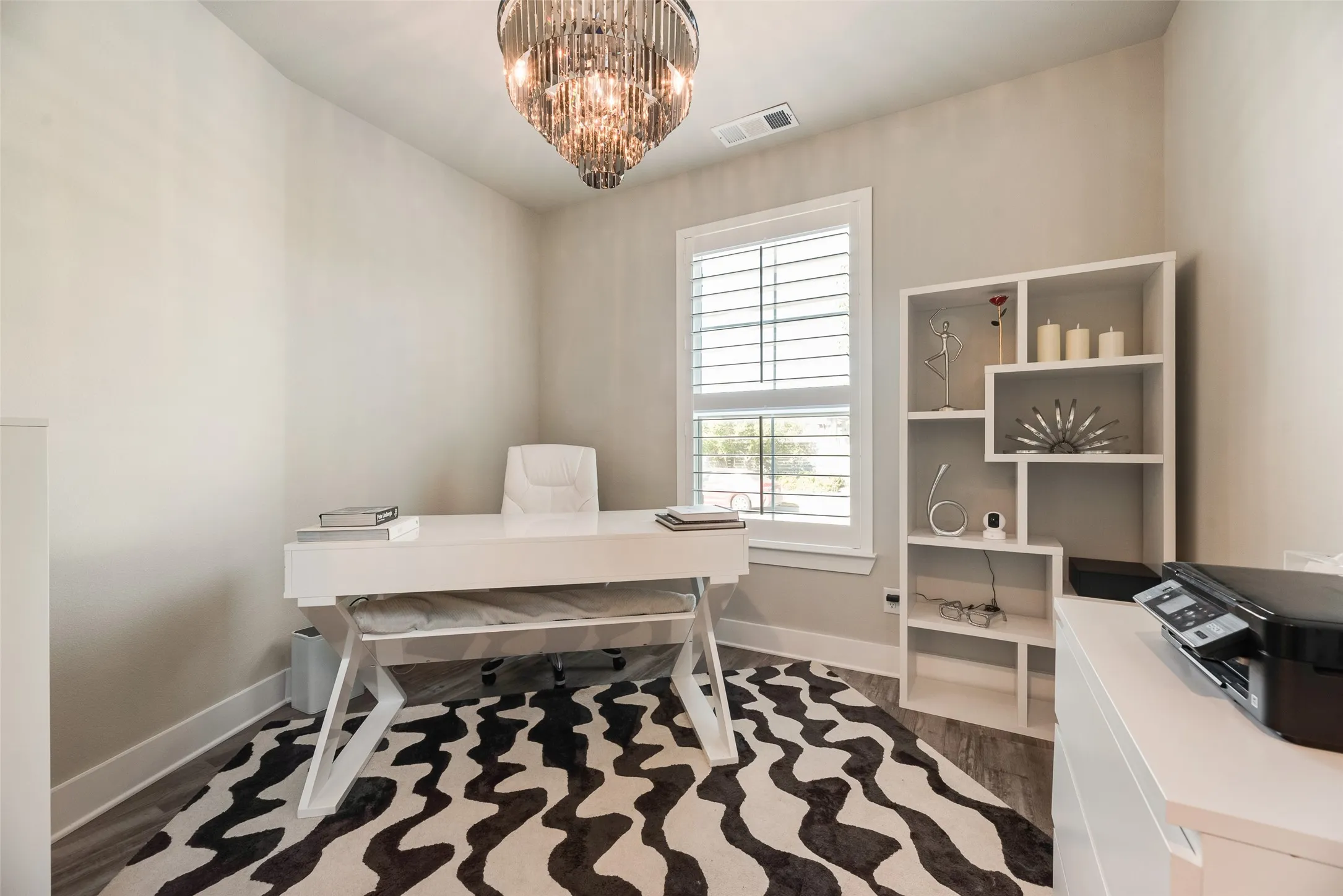 Chandelier lighting fixture, light gray wall tones, window with interior shutters, wood-finish flooring, and built-in shelving