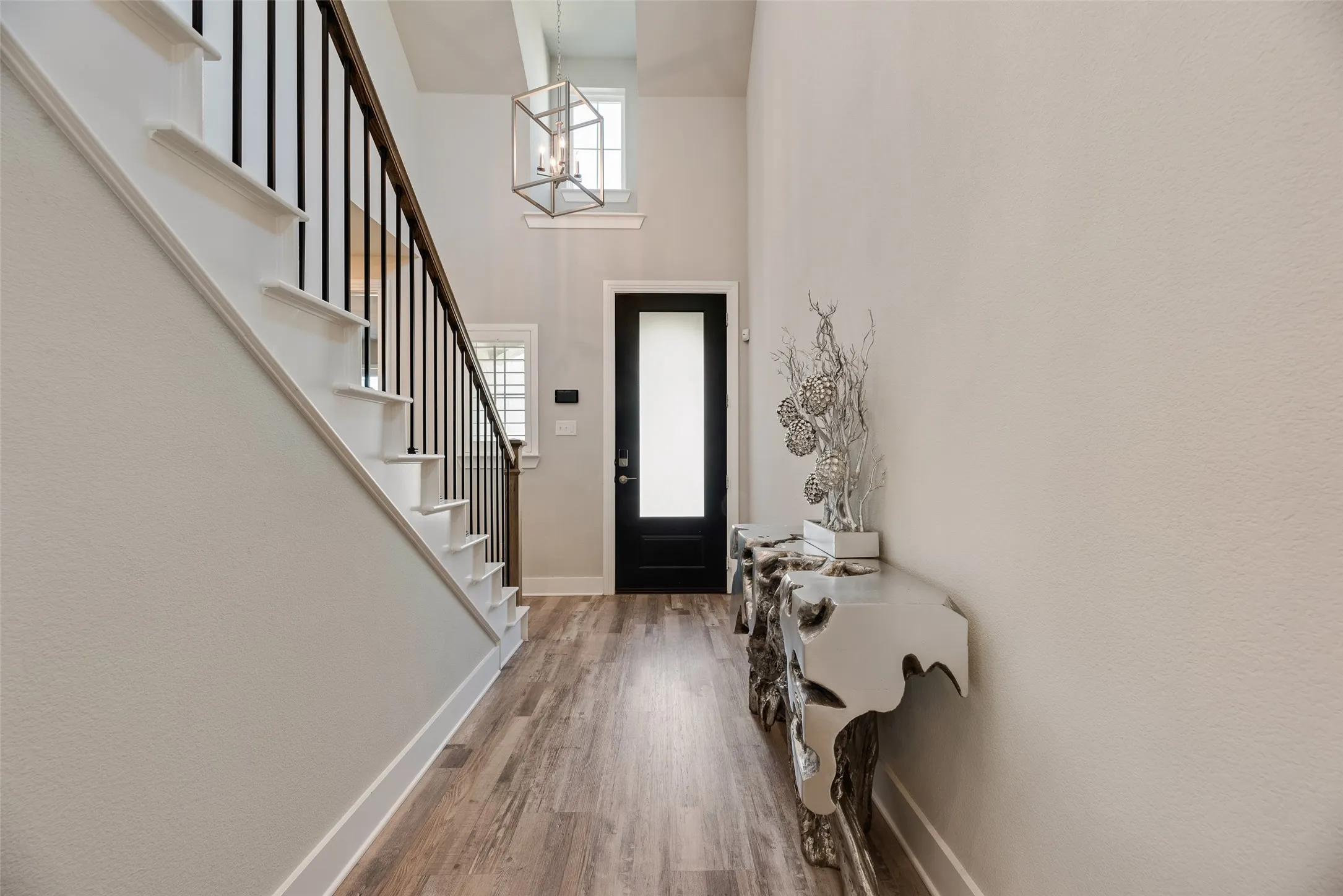 Wood-finish flooring extending through the entryway, complemented by a prominent staircase with dark metal balusters and a wood handrail