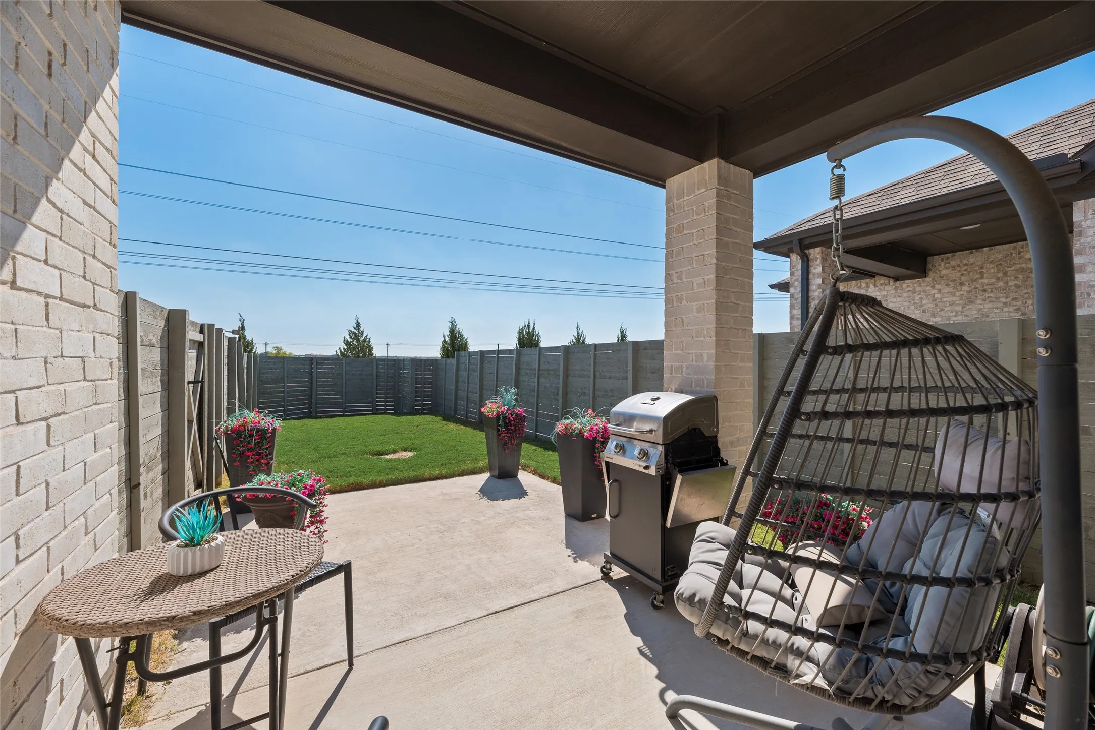 Covered patio with concrete flooring, brick column, and a fenced backyard featuring a manicured lawn