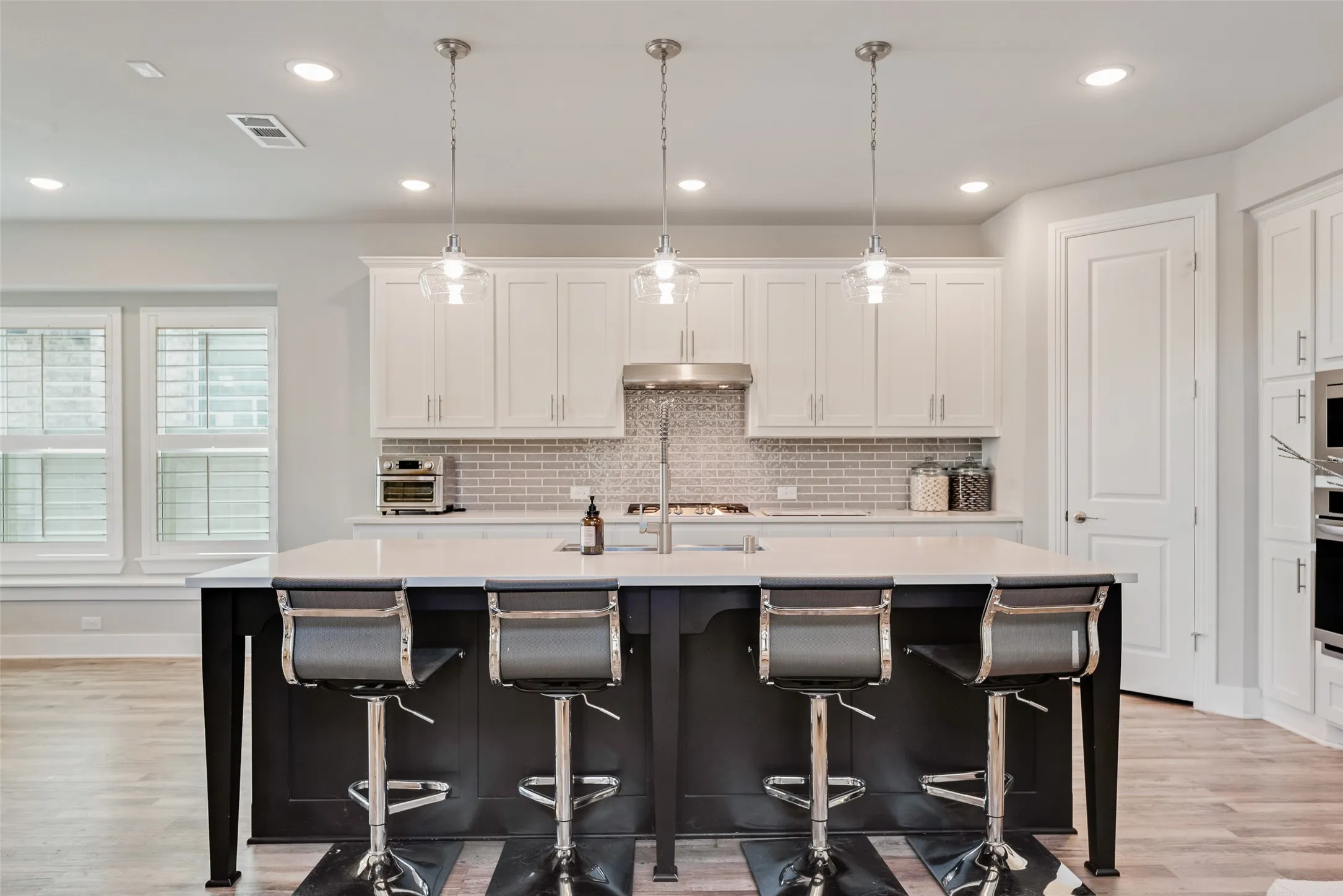 Kitchen featuring a large island with white countertop, white upper and lower cabinetry, stainless steel appliances, and wood-finish flooring