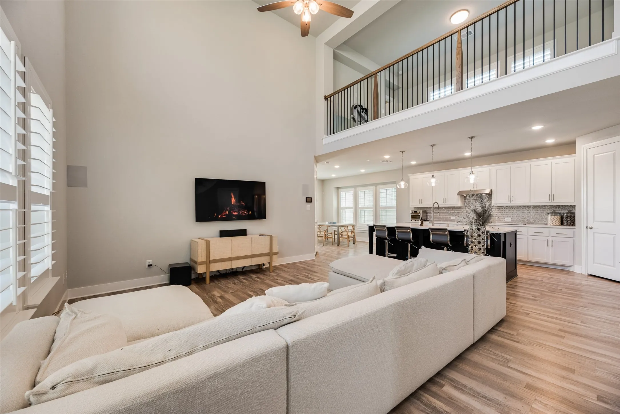 Two-story great room with soaring ceilings, wood-finish flooring, and a second-story overlook with a wrought iron railing
