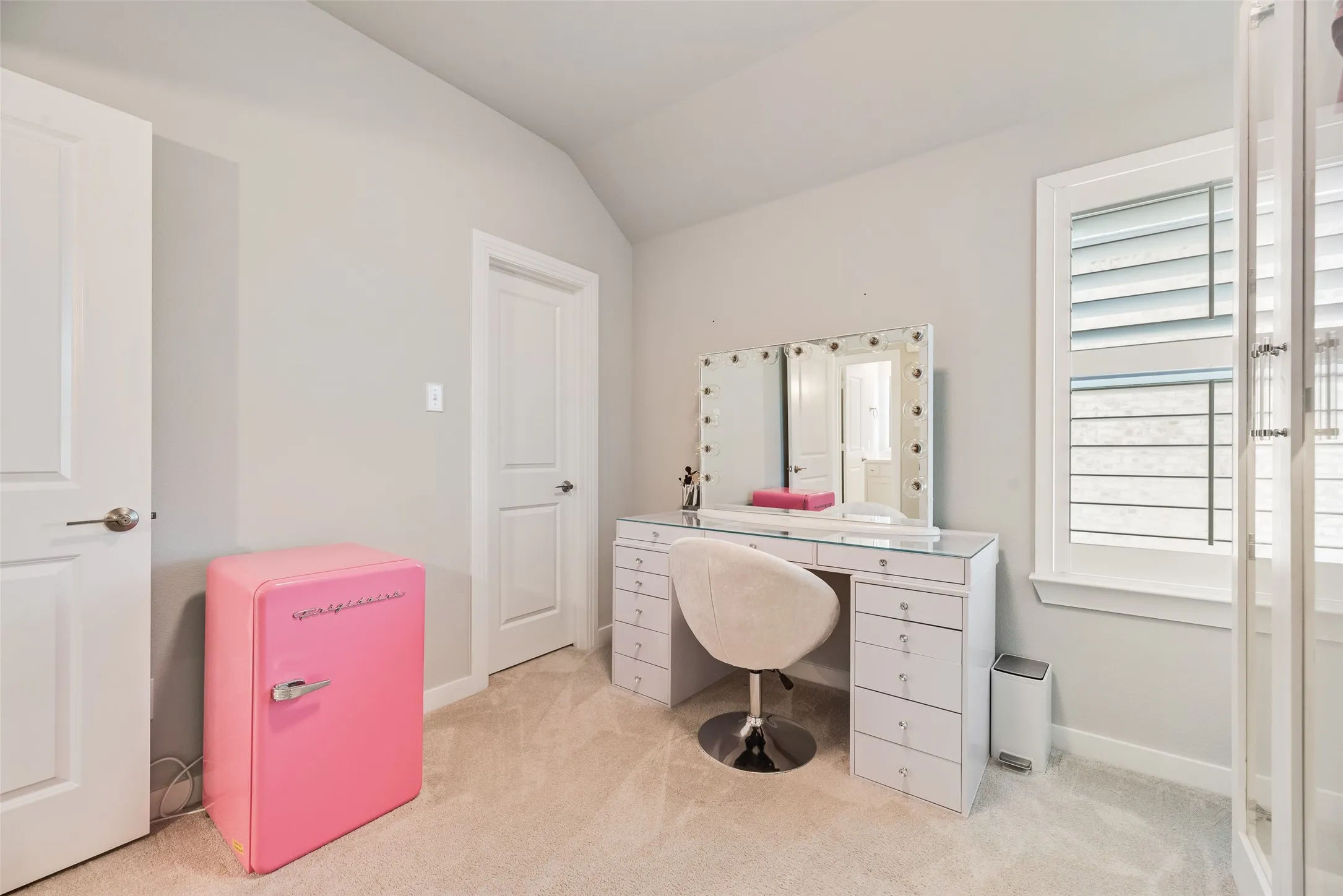 Vaulted ceiling, two paneled doors, carpeted flooring, and a window with plantation shutters