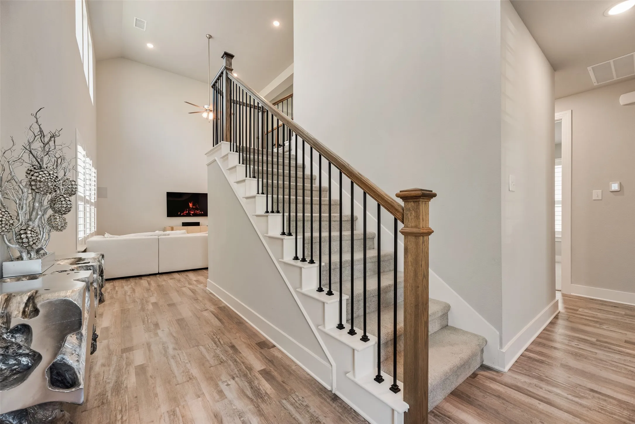 High vaulted ceiling, wood-finish flooring, staircase with wrought iron balusters, natural wood handrail, and shuttered windows