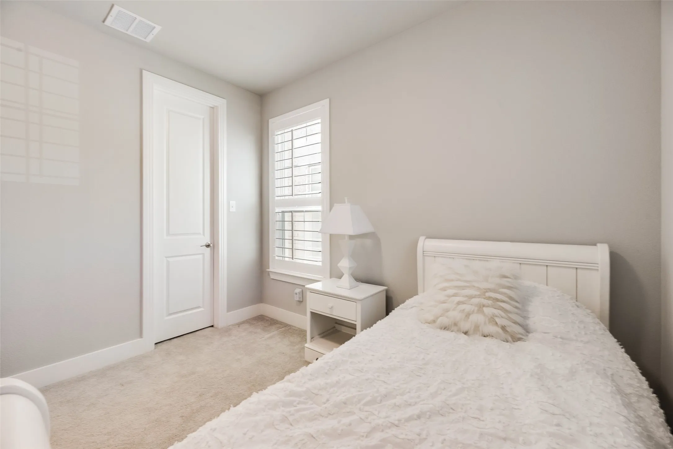Neutral wall color with plush carpet flooring, white paneled door, and window featuring louvered shutters