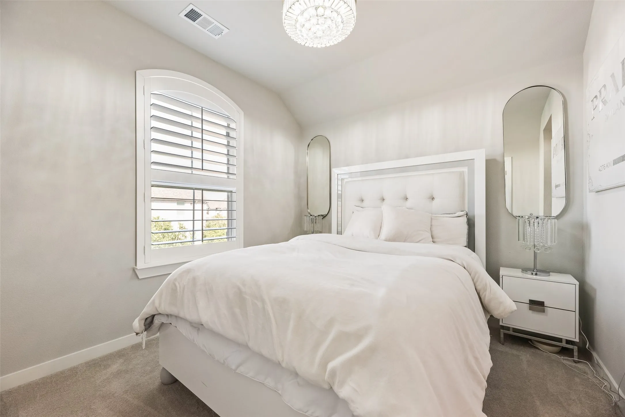 Arched window with louvered shutters, wall-to-wall carpeting, and a crystal chandelier