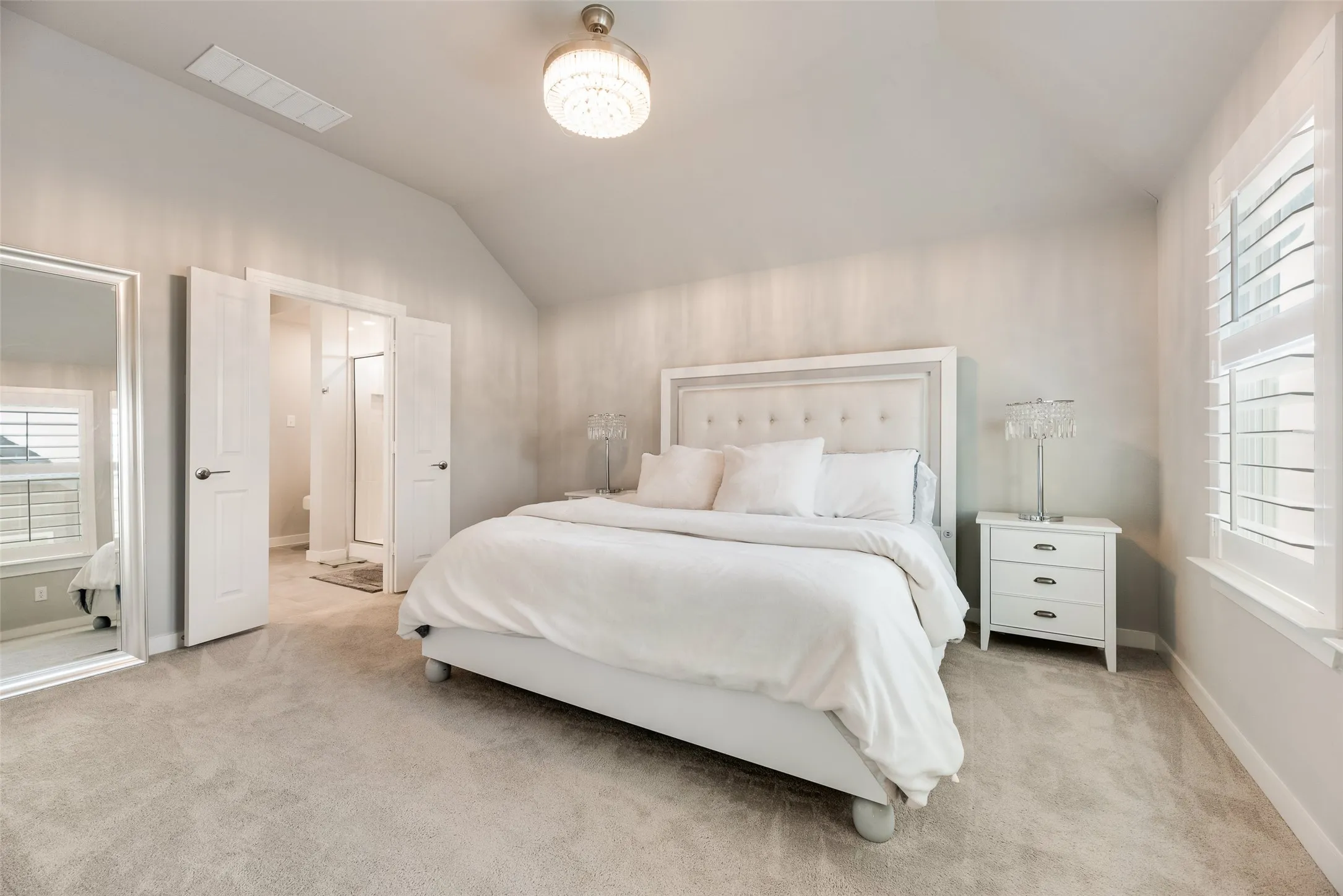 Vaulted ceiling with an attached light fixture, plush carpet flooring, white interior doors, and window with white plantation shutters