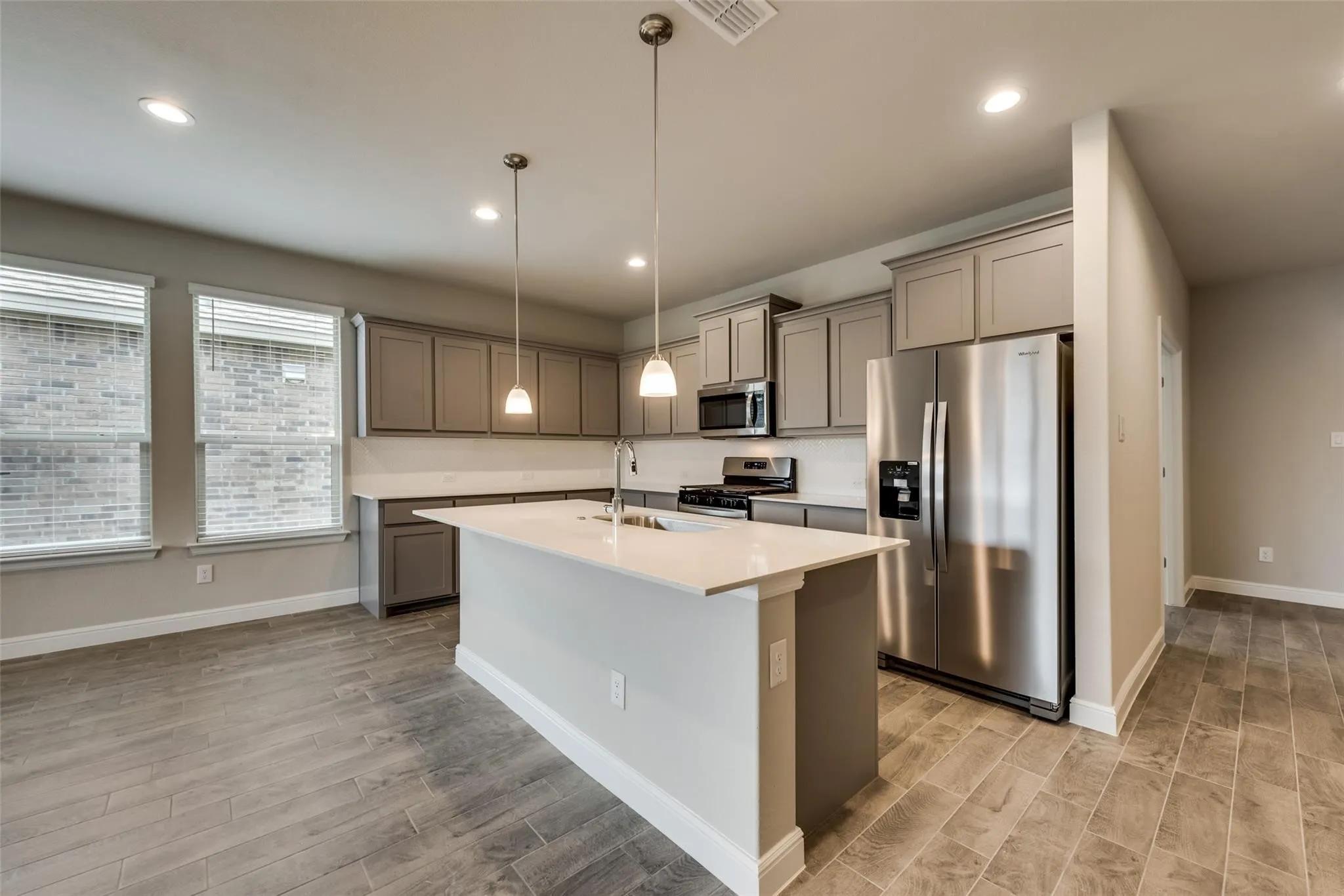 Kitchen featuring light hardwood / wood-style flooring, stainless steel appliances, sink, hanging light fixtures, and an island with sink
