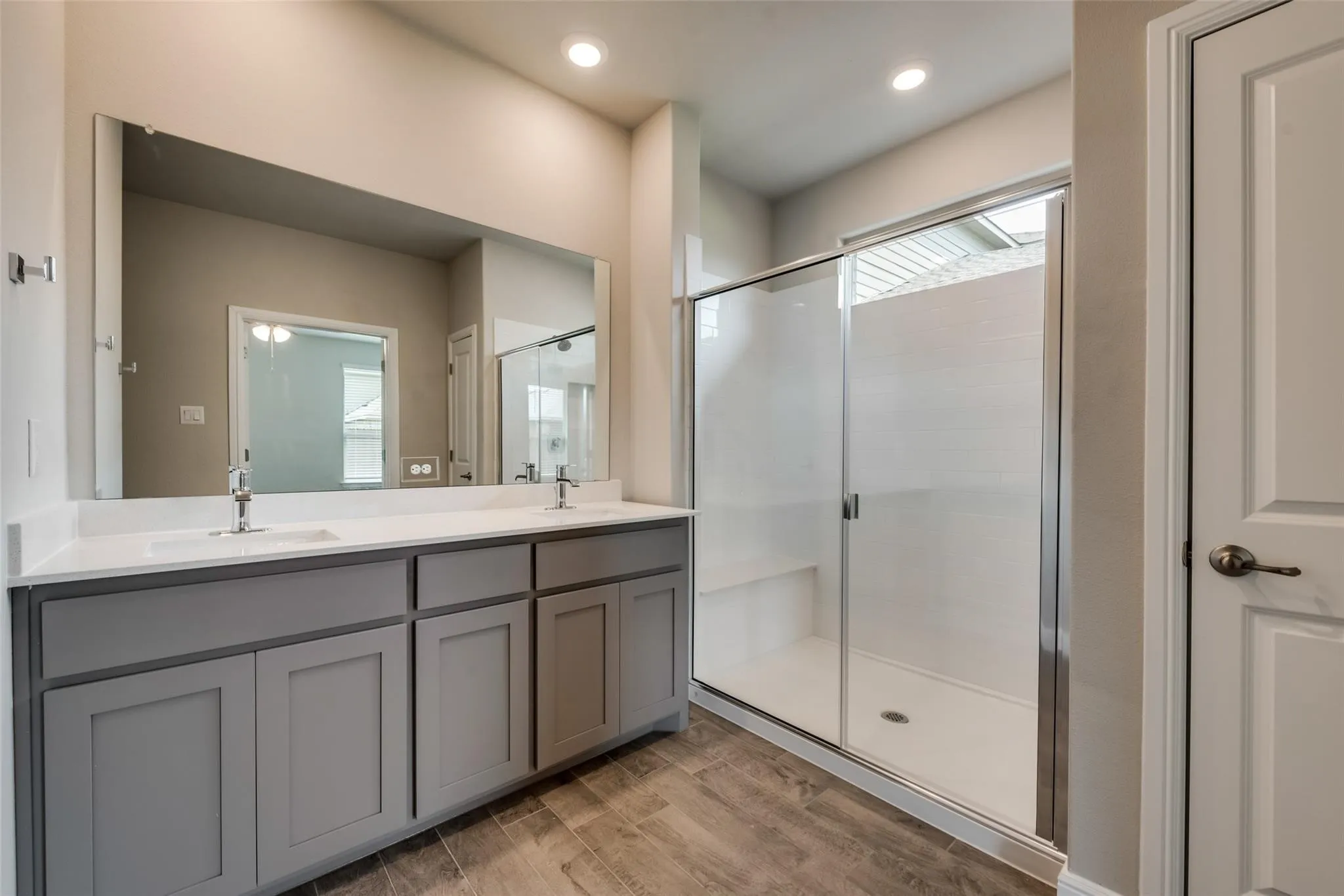 Bathroom featuring dual vanity, a shower with shower door, and wood-type flooring