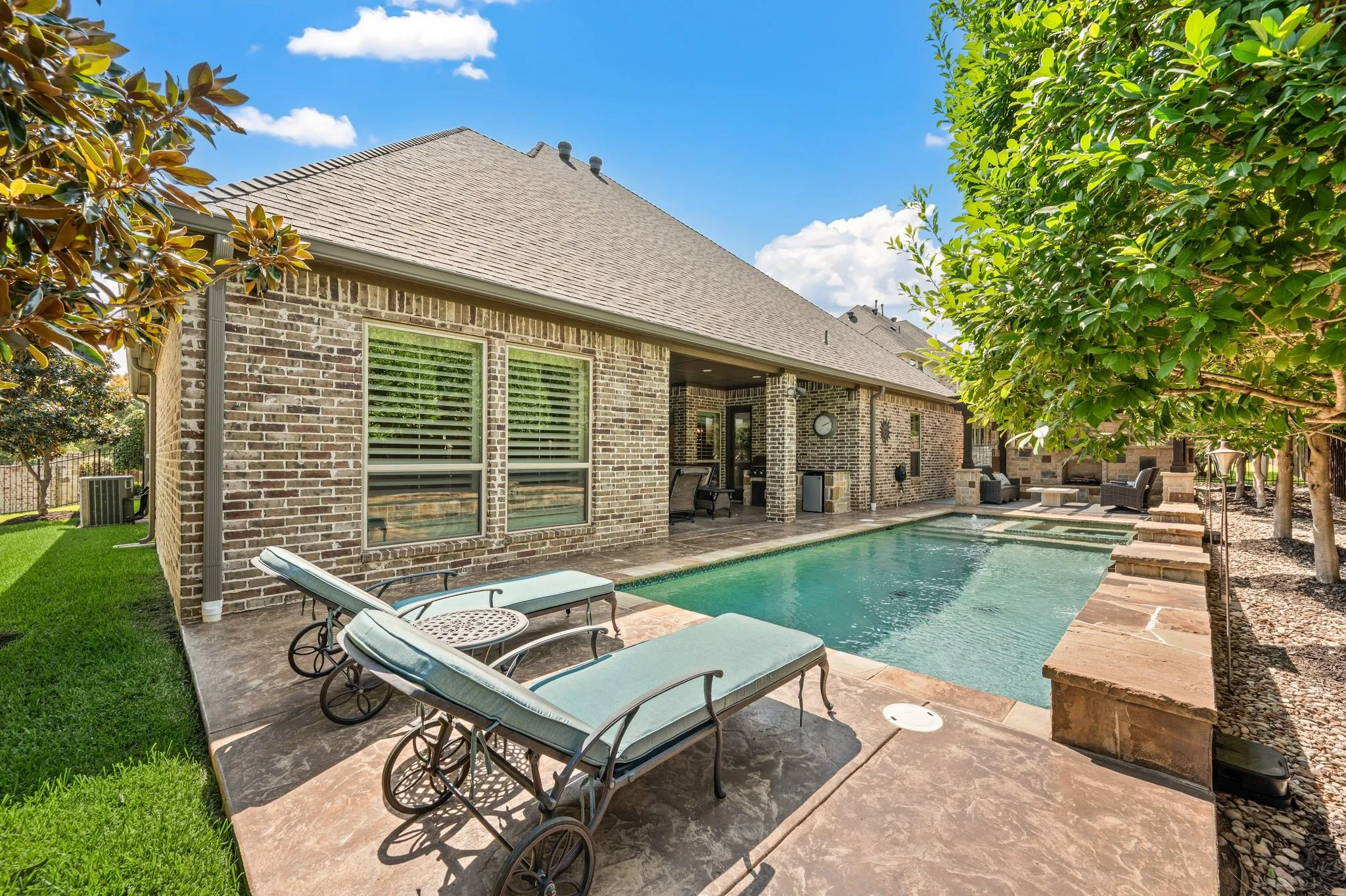 Brick exterior with covered patio, integrated swimming pool, spa, and stone hardscaping