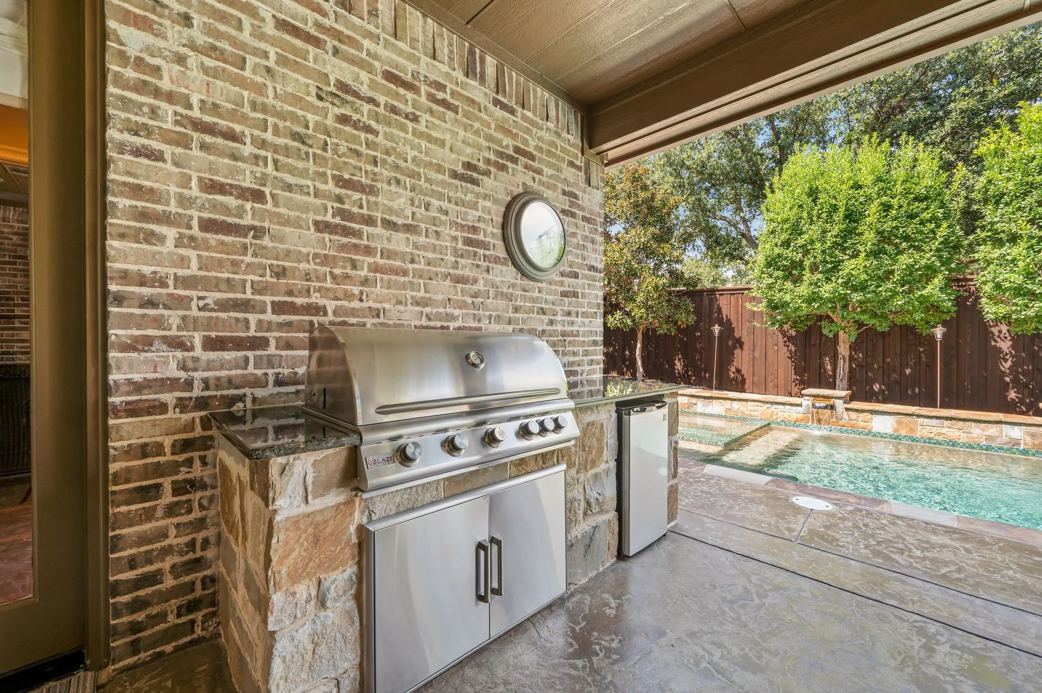 Covered patio with an outdoor kitchen featuring a built-in stainless steel grill and refrigerator
