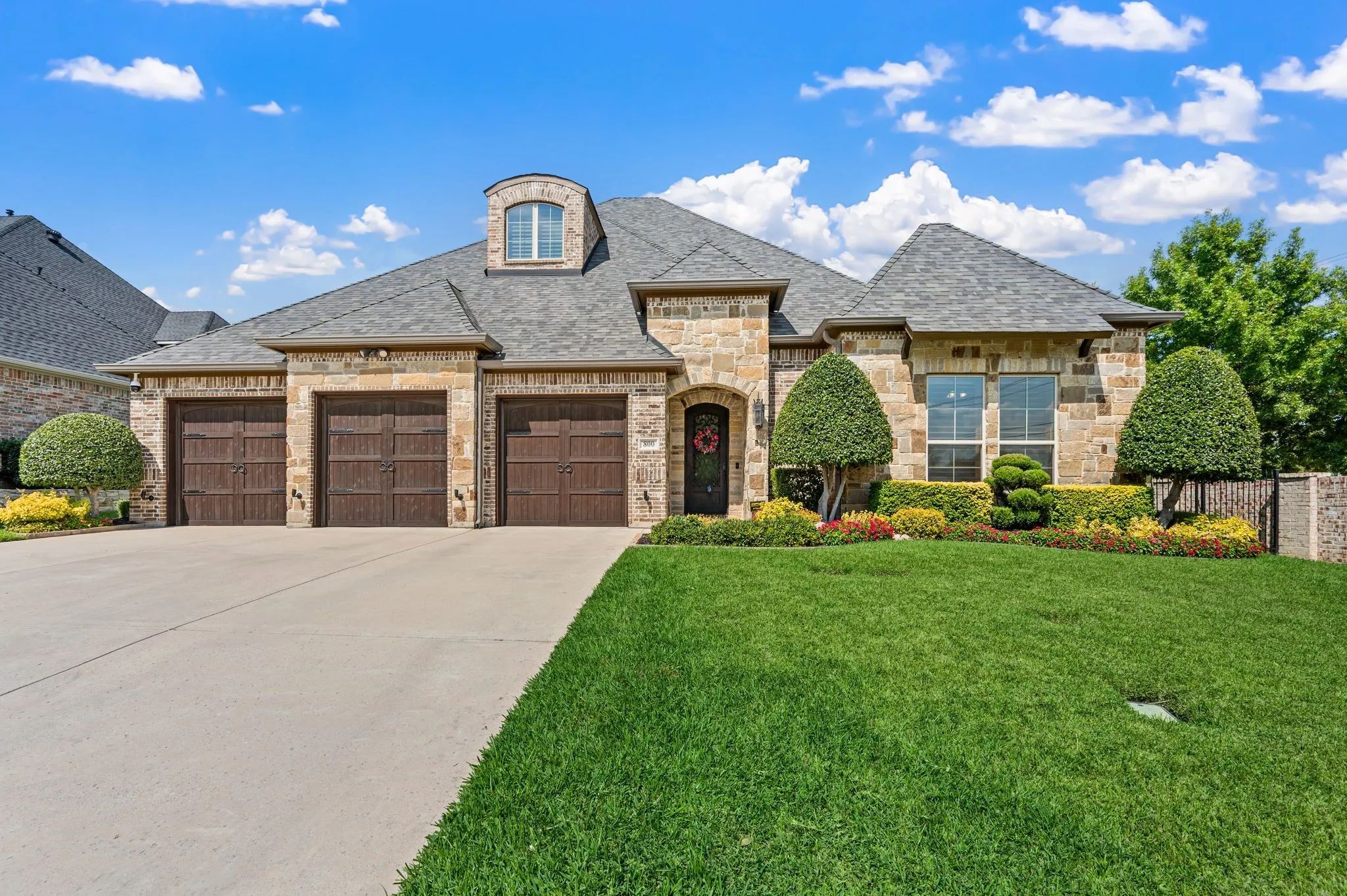 Stone exterior with a three-car garage, dormer window, and mature landscaping