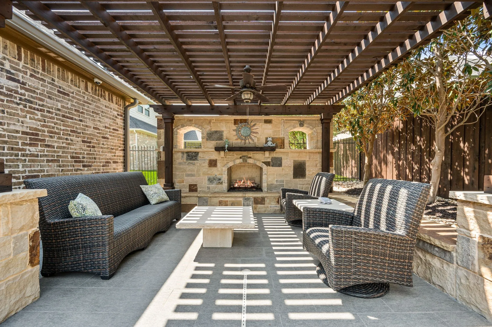 Covered patio with a wooden pergola, built-in stone fireplace, ceiling fan, and stone accent walls