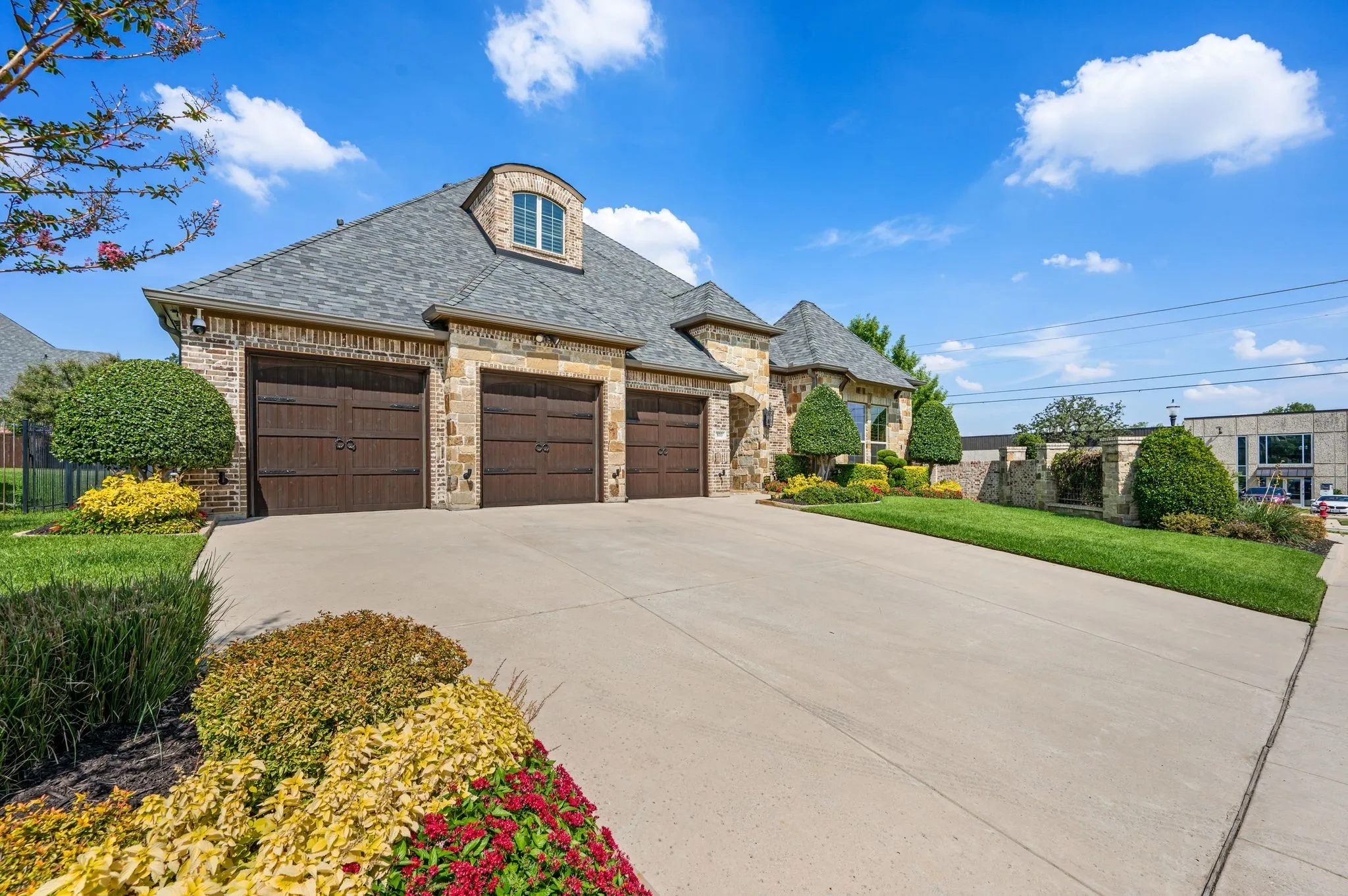 Stone and brick exterior with a multi-car garage, dormer window, concrete driveway, and landscaped front yard