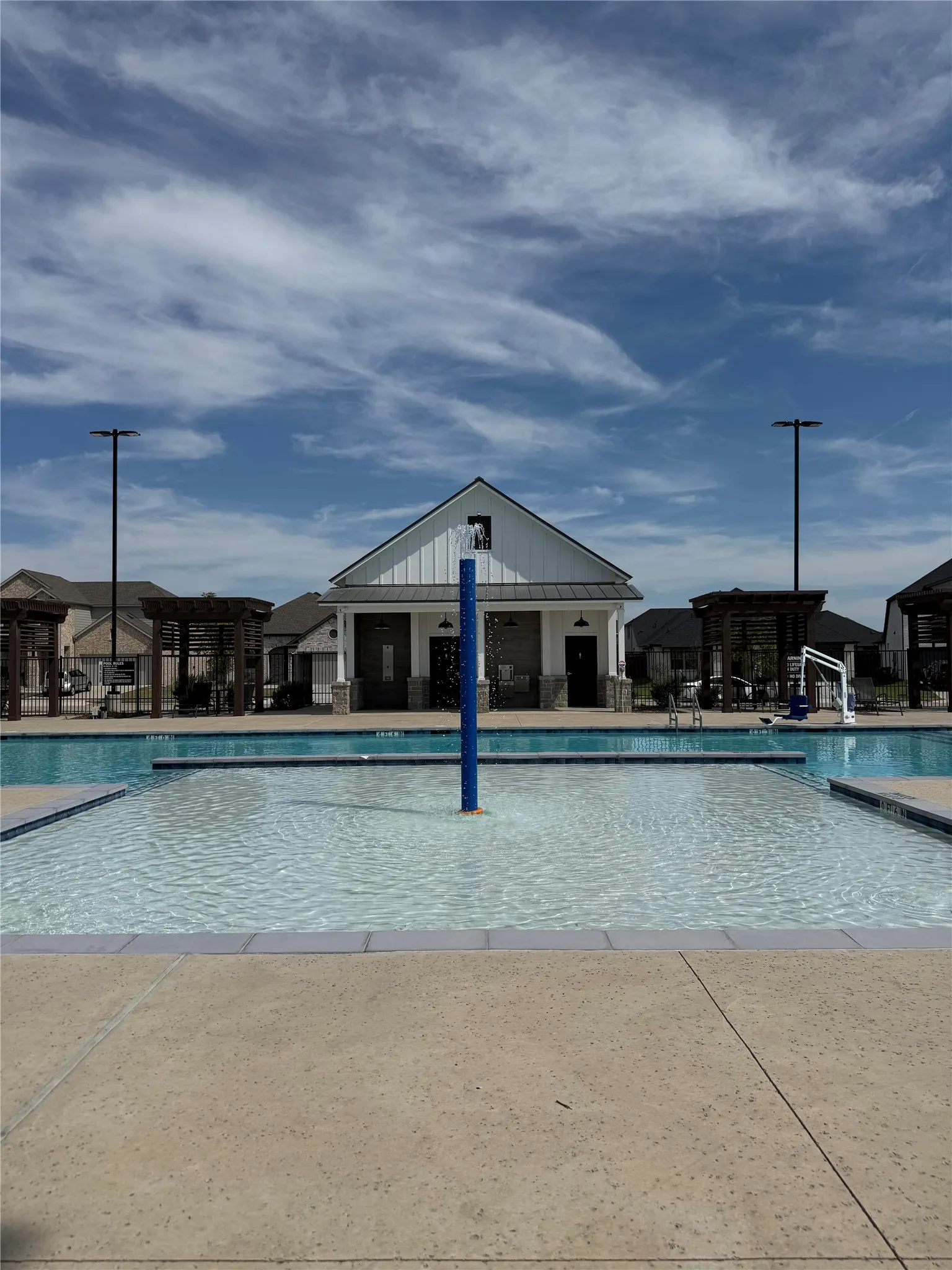 Outdoor swimming pool with shallow entry, adjacent concrete deck, and a clubhouse with a gabled roof and board-and-batten siding