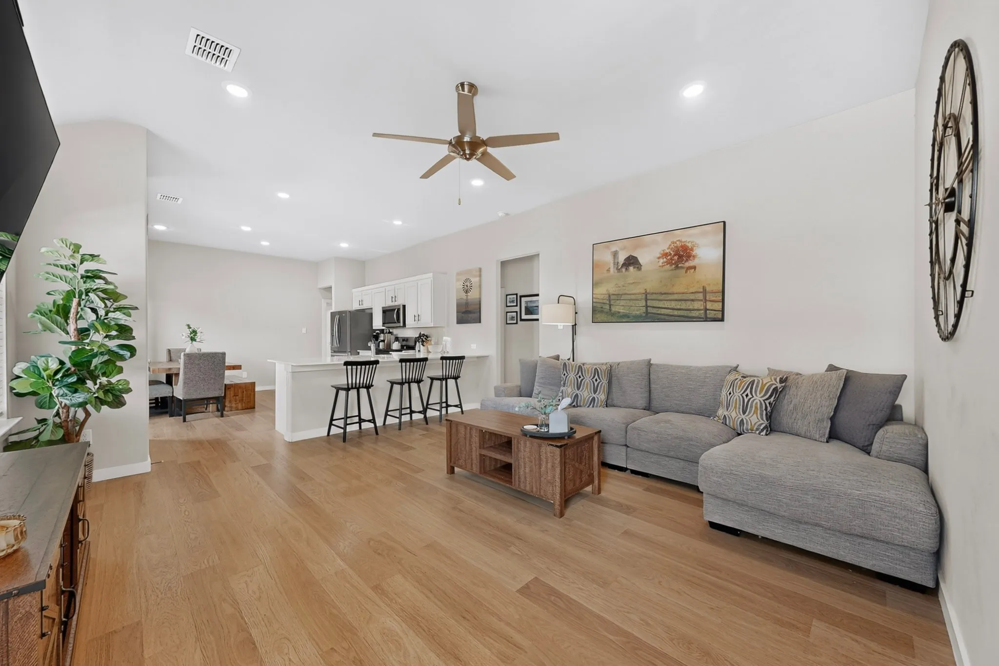 Wood-finish flooring throughout, recessed lighting, ceiling fan, kitchen island with counter seating, and white cabinetry