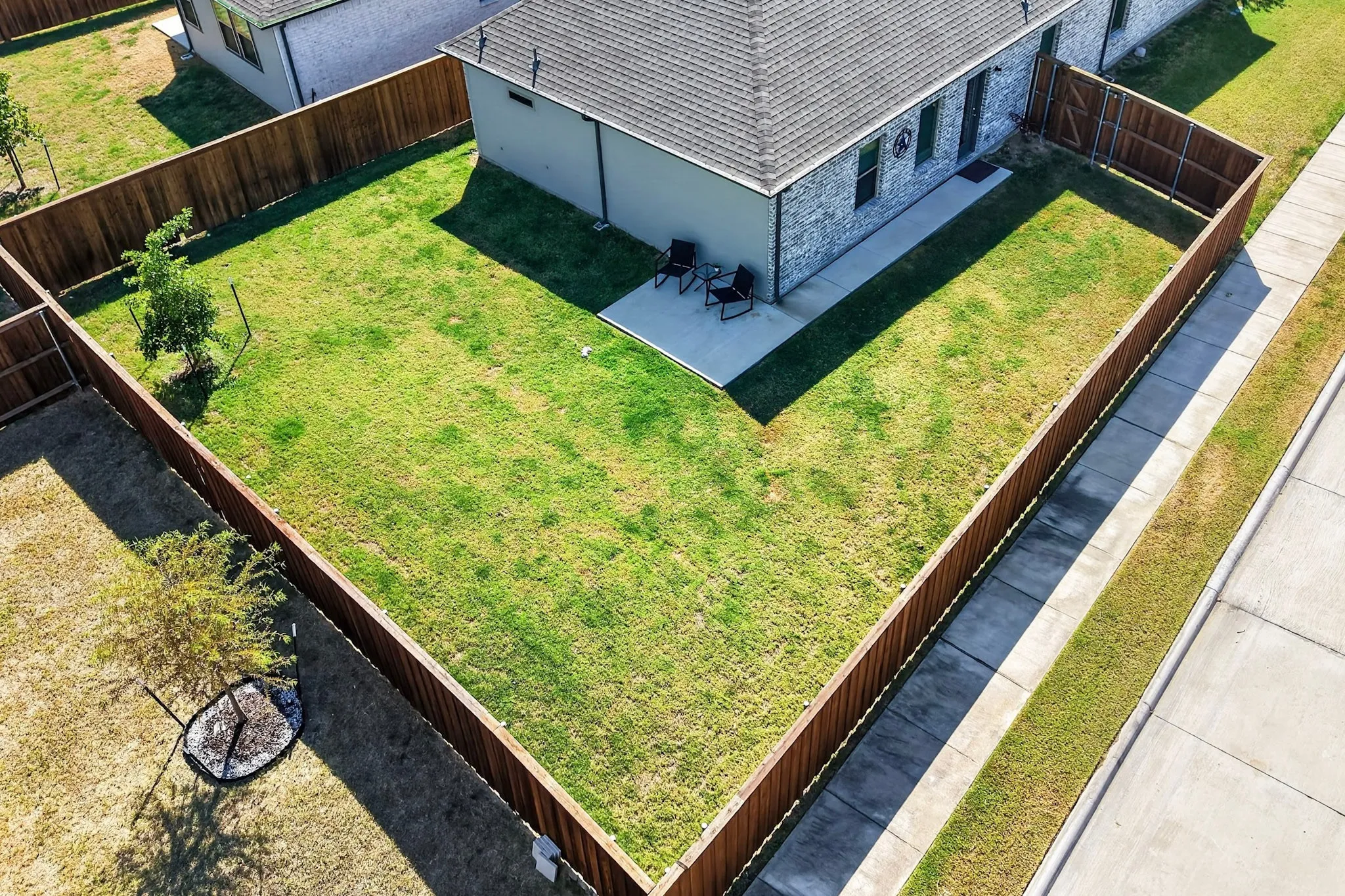 Spacious enclosed backyard featuring a concrete patio, wood privacy fencing, and a grassy area