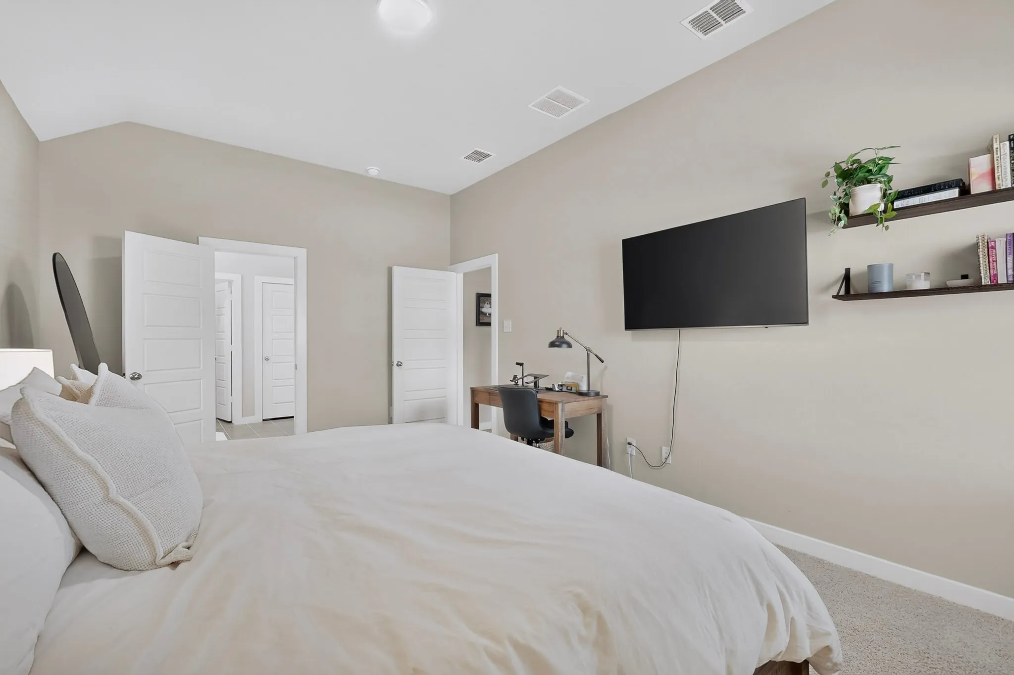 Vaulted ceiling with flush-mount lighting, neutral wall tones, carpeted flooring, and built-in wall shelving