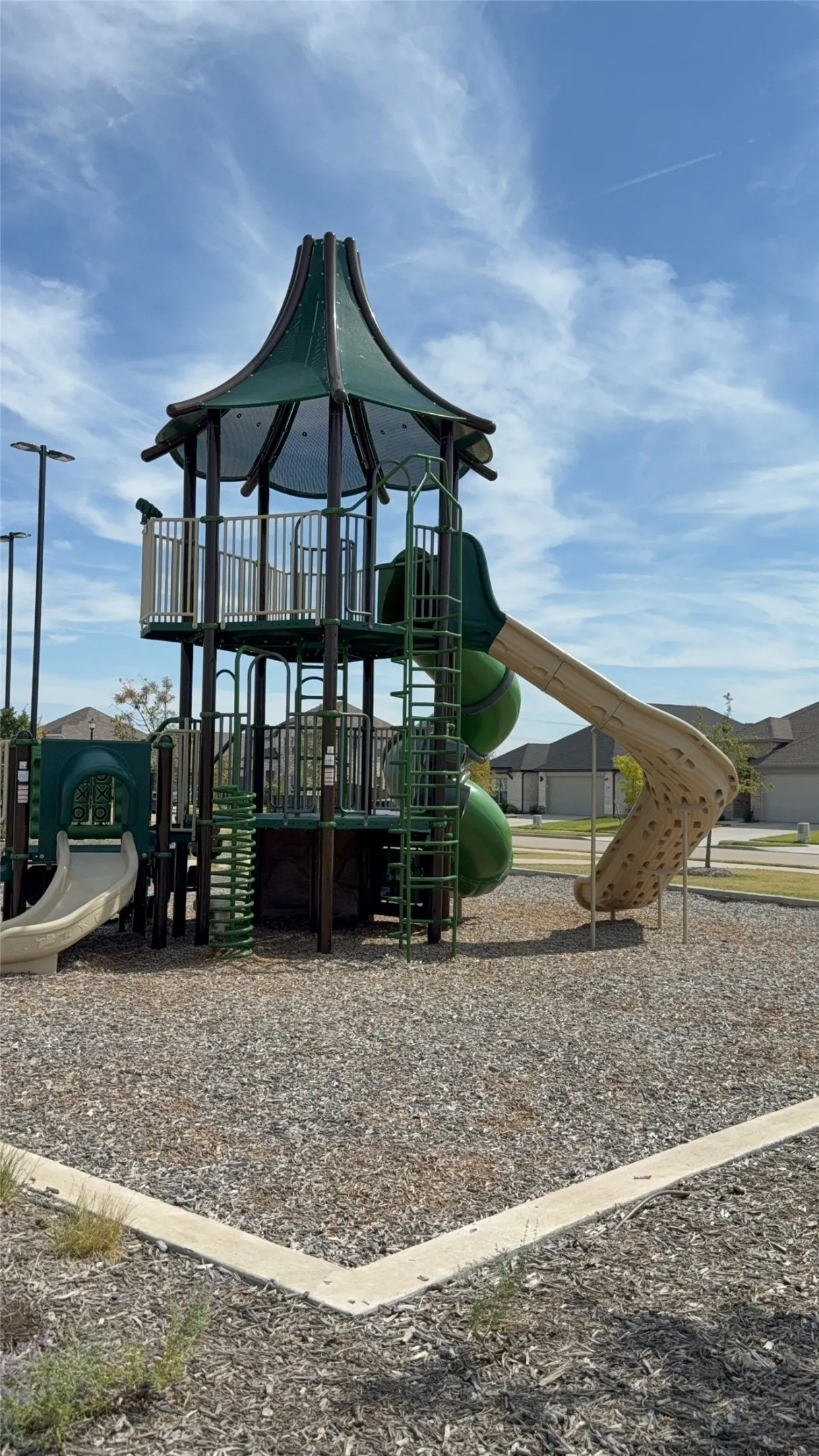 Play structure with multiple slides, climbers, and platforms, set on a wood chip surface with concrete edging