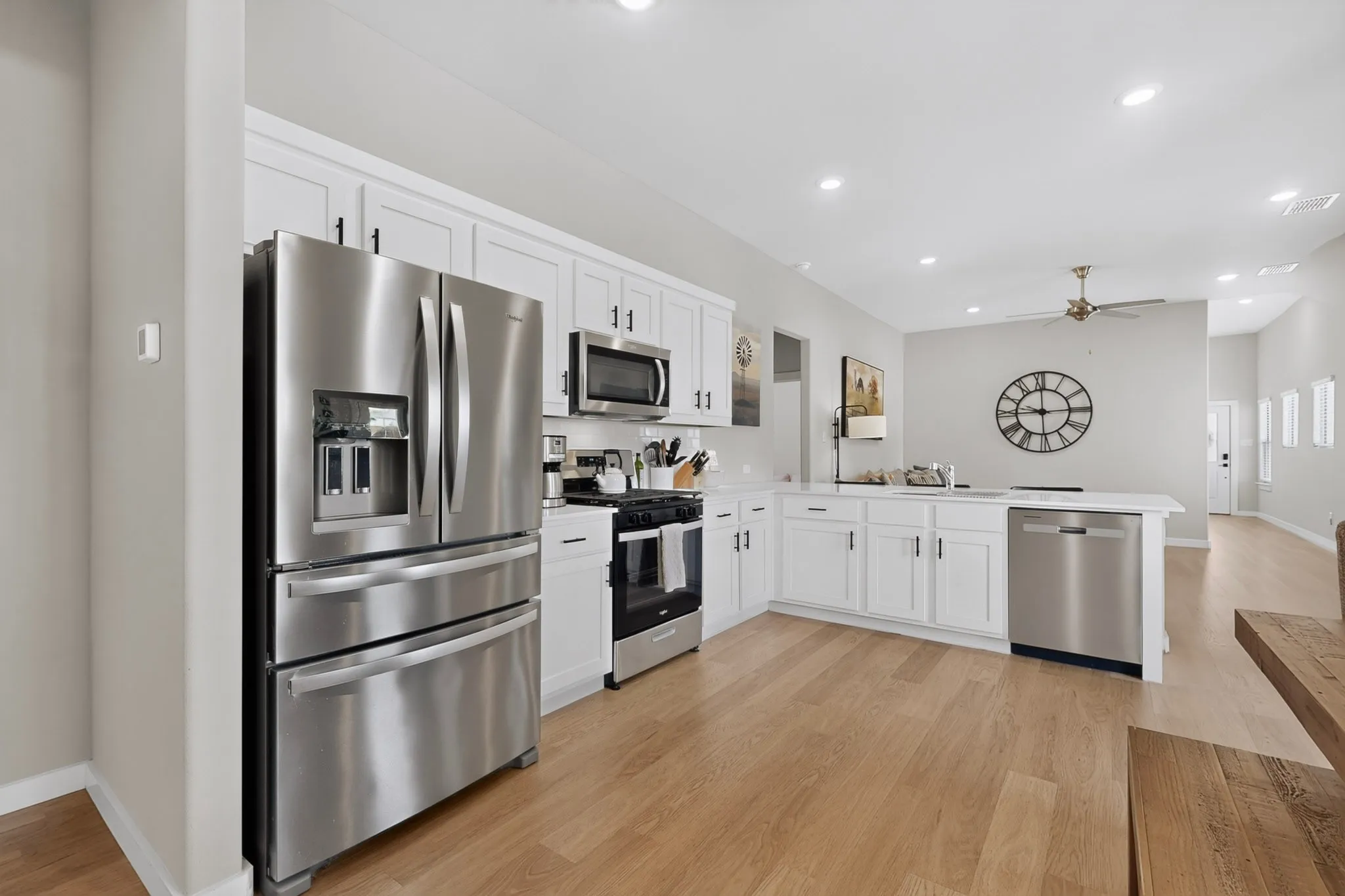 Open-concept kitchen featuring white cabinetry, stainless steel appliances, recessed lighting, wood-finish flooring, and a ceiling fan