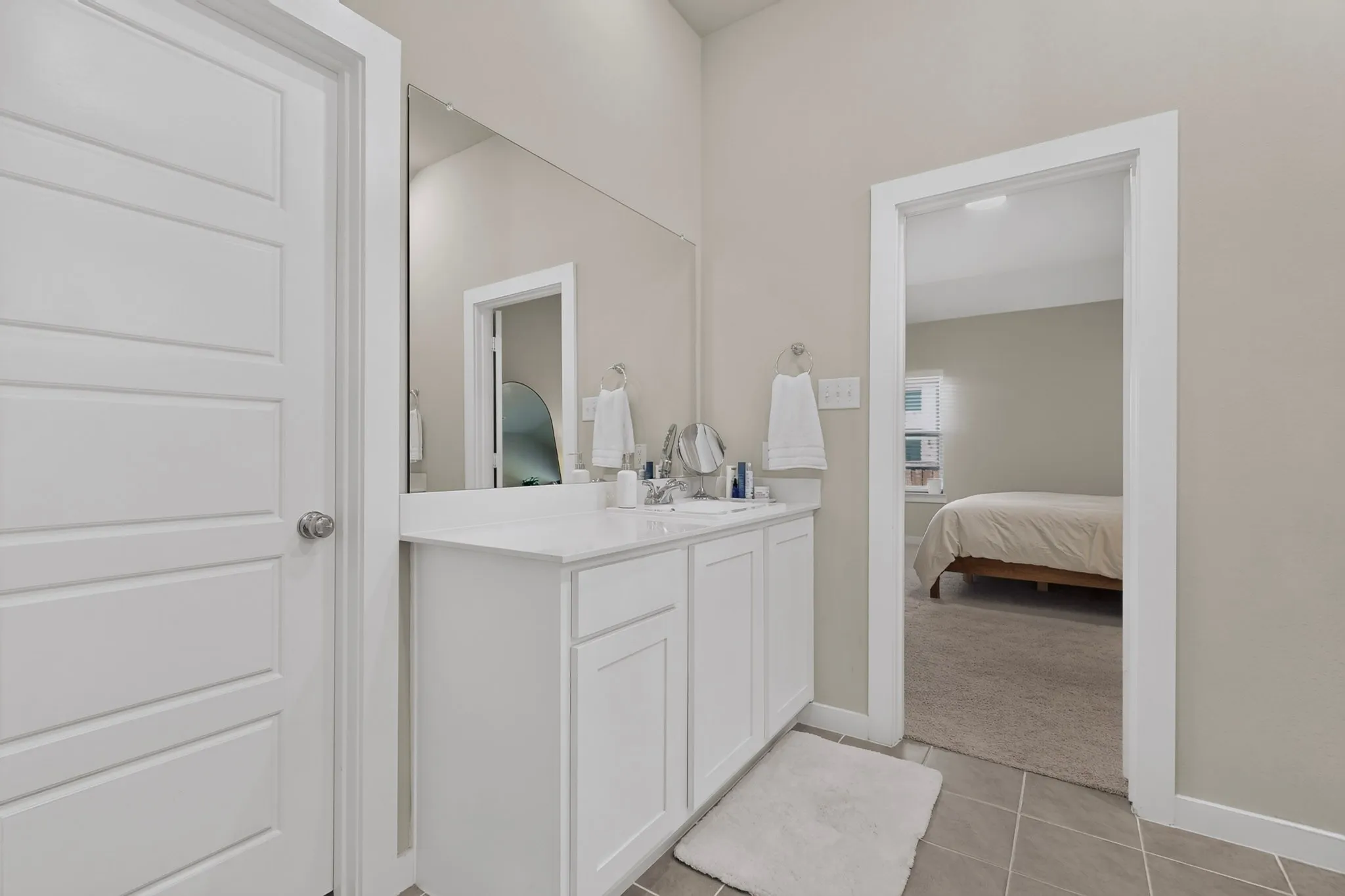 White vanity with a single basin, expansive wall-mounted mirror, and tile flooring