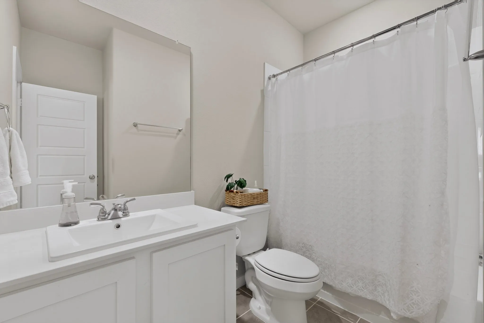 Shower tub combo, White vanity with integrated sink, chrome faucet, wall-mounted mirror, and tile flooring