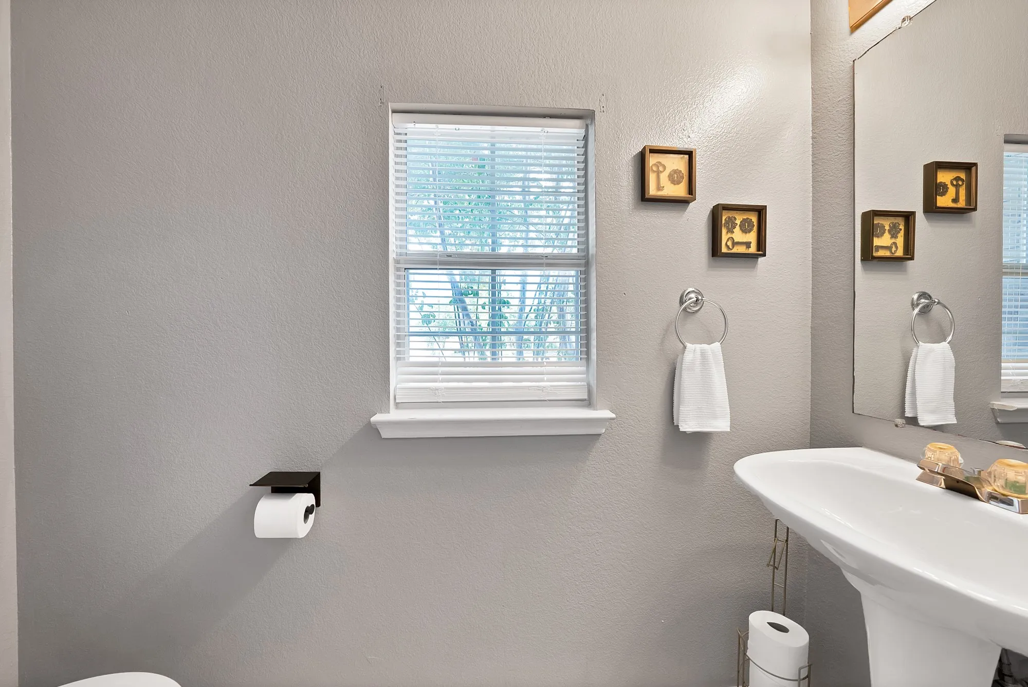 Pedestal sink with chrome fixtures, window with blinds, and a wall-mounted mirror