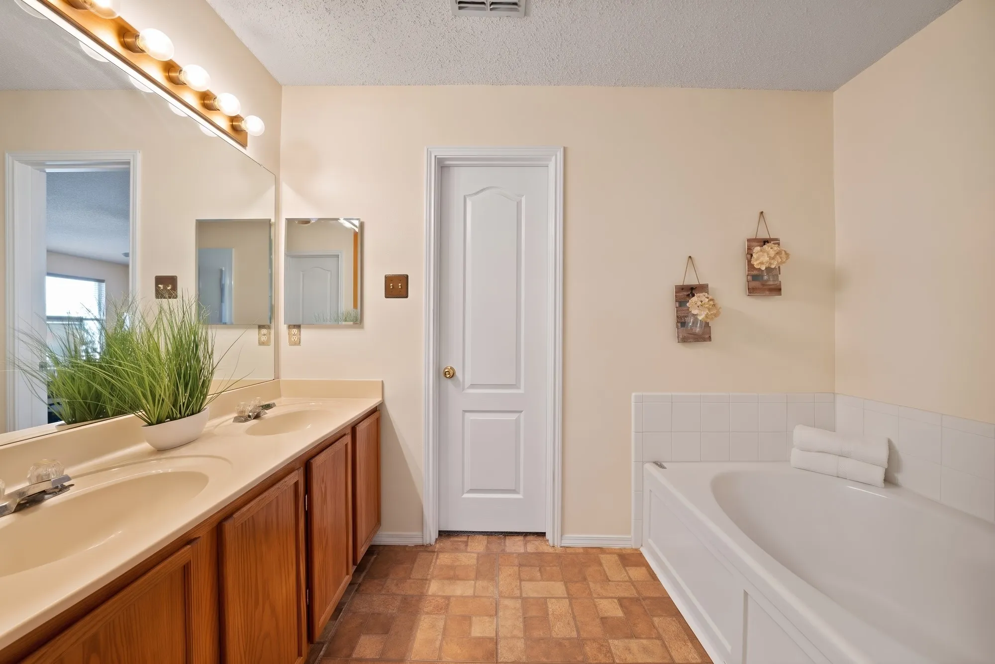 Double vanity with integrated sinks, wood-finish cabinetry, built-in bathtub with tiled surround, and a panel-style door