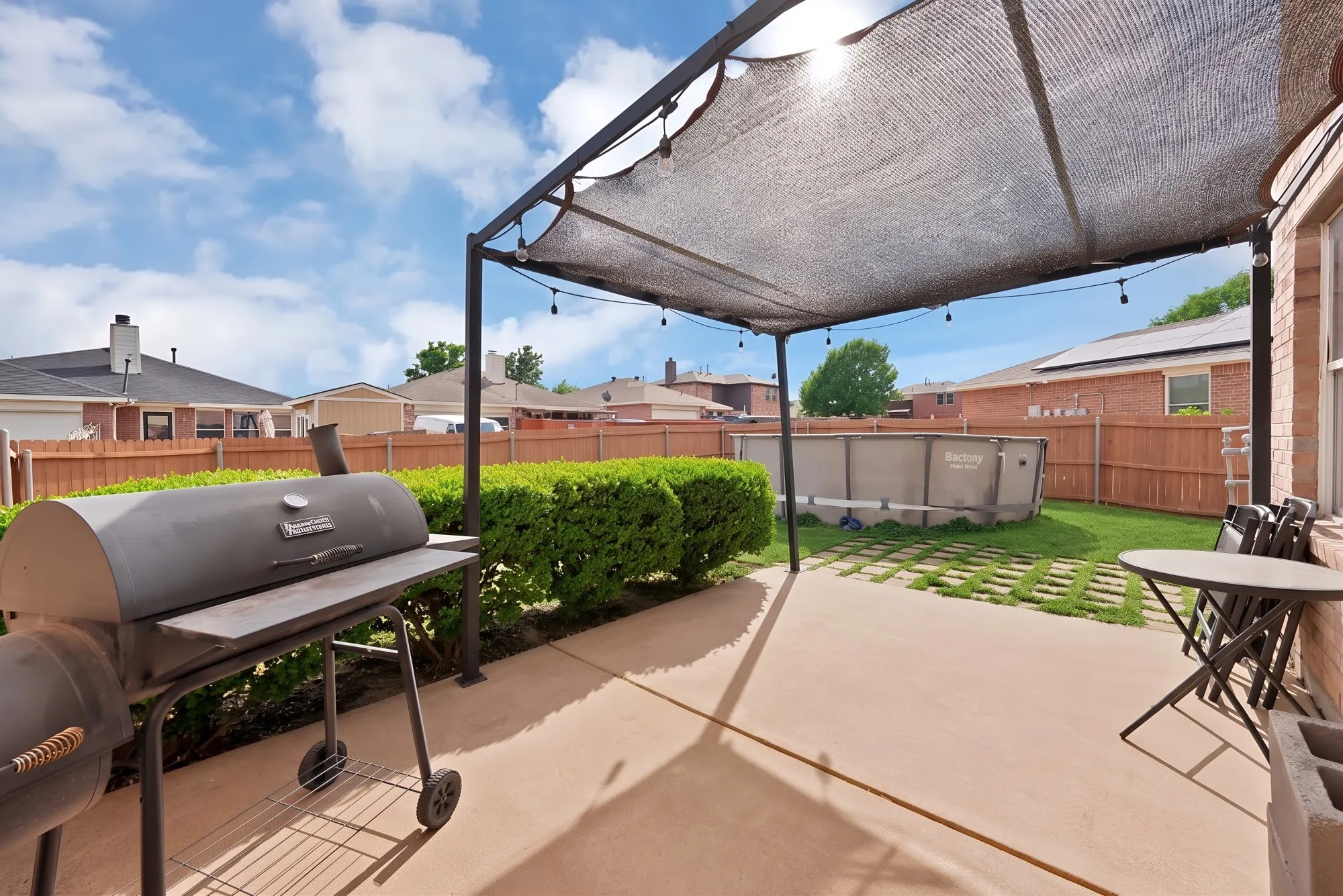 Spacious concrete patio with a shade structure, manicured hedges, and a fenced perimeter