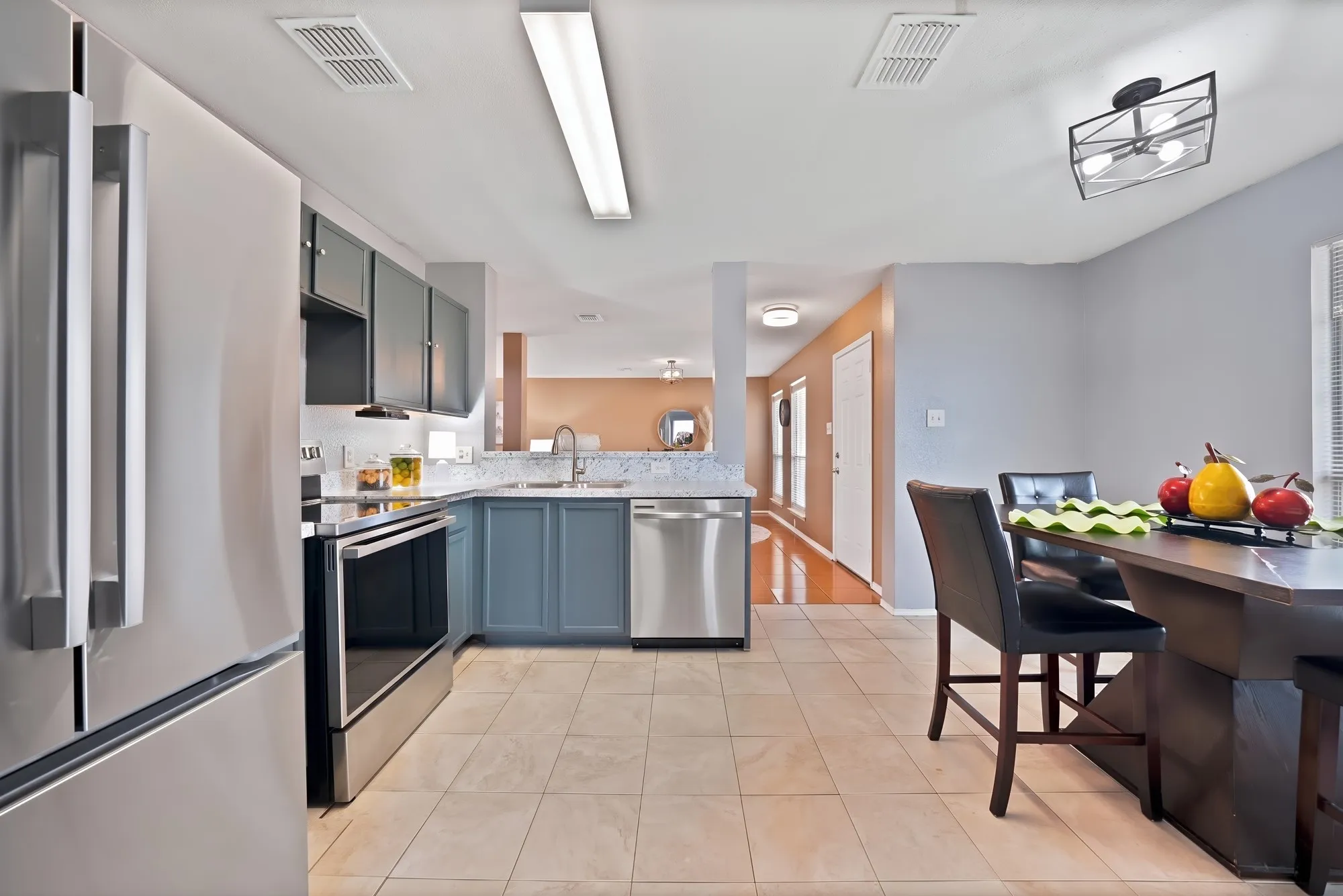 Kitchen featuring stainless steel appliances, two-tone cabinetry, tiled flooring, and a dining area with a contemporary light fixture