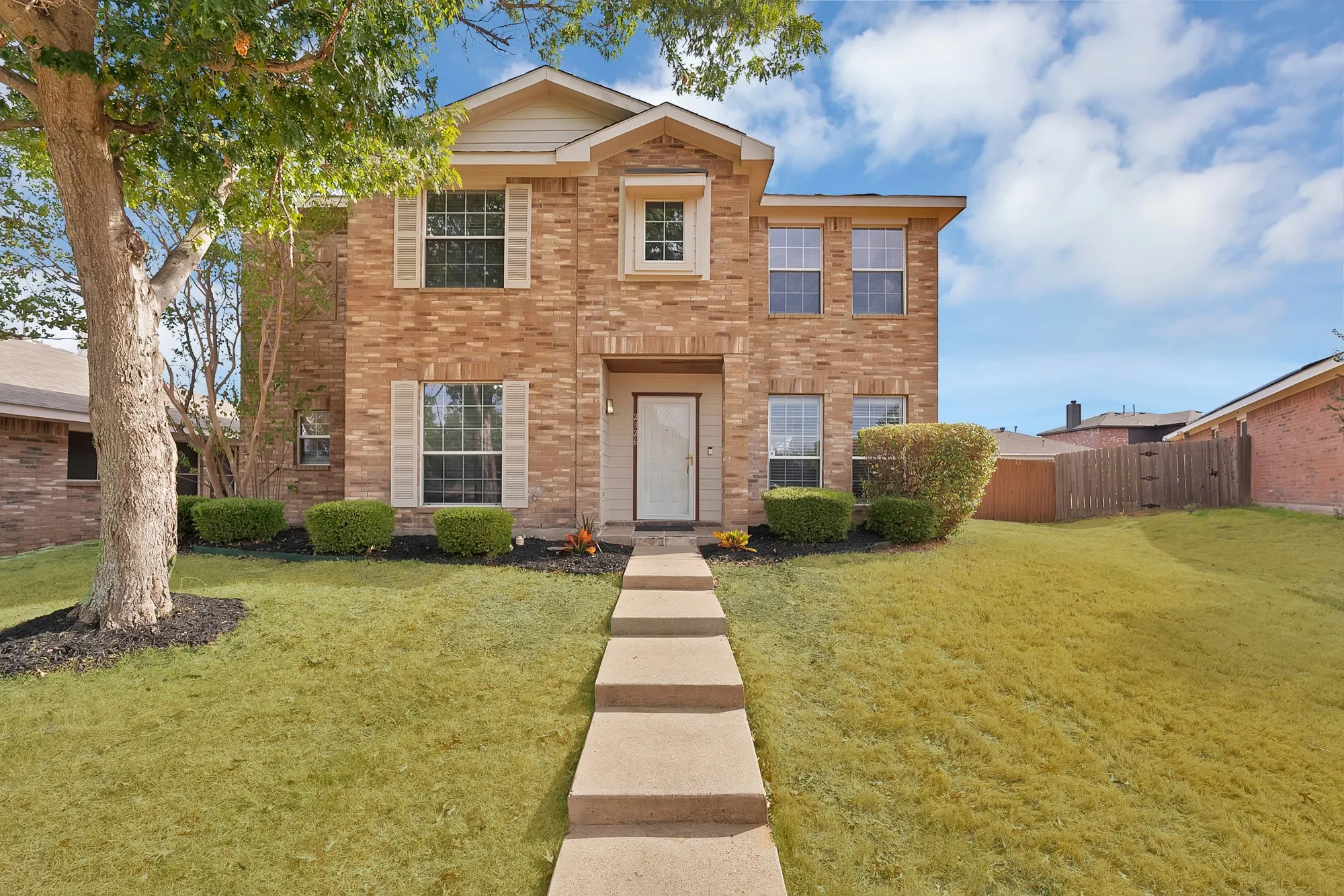 Two-story brick exterior with light-colored shutters, a prominent front entry, a concrete walkway, and established landscaping