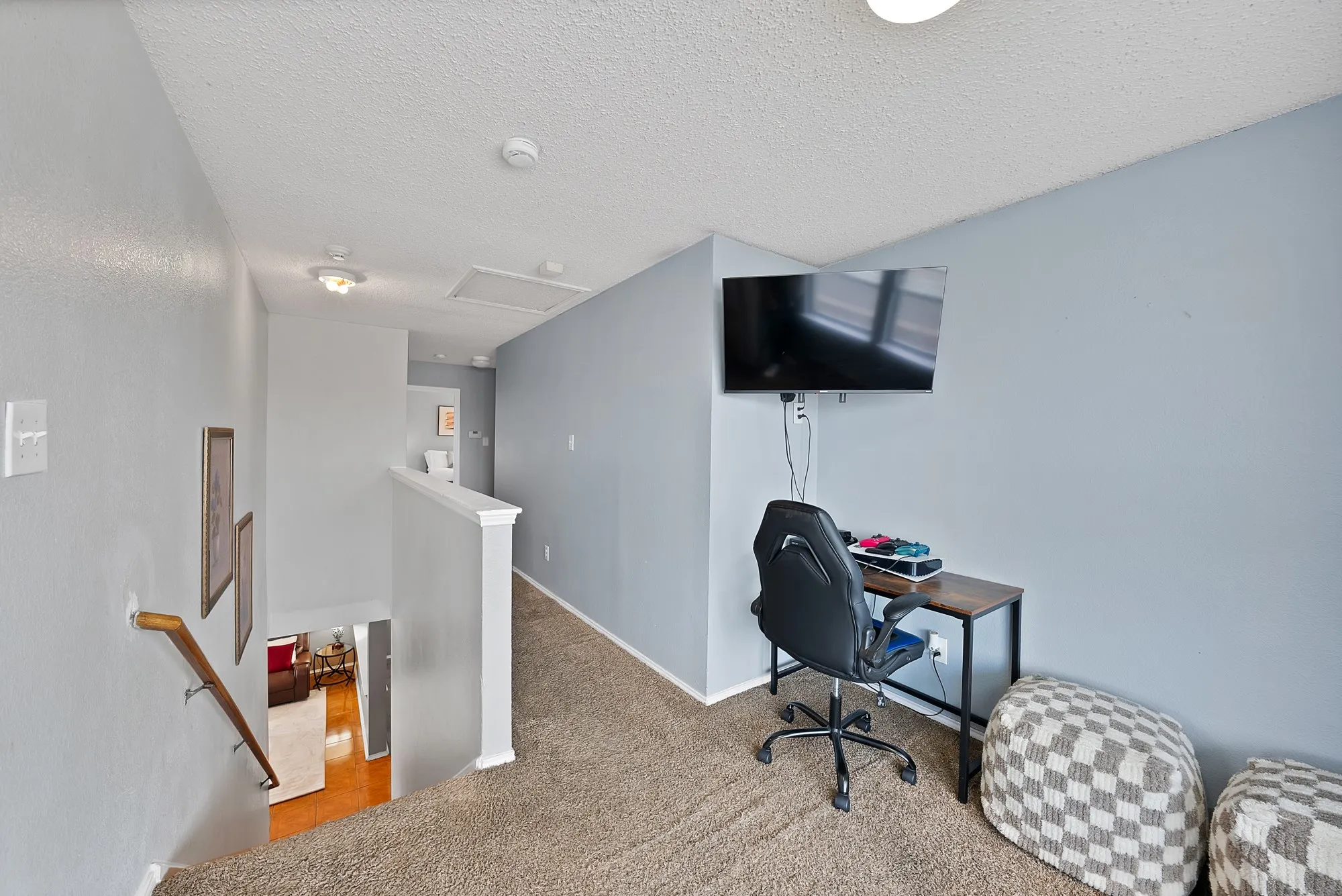 Carpeted upper-level landing with painted walls, a built-in wall-mounted television, a white banister, and an overhead light fixture