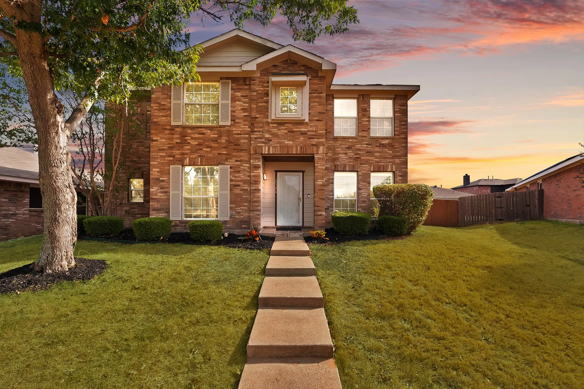 Brick façade, gabled roofline, concrete walkway, mature landscaping, and front entry