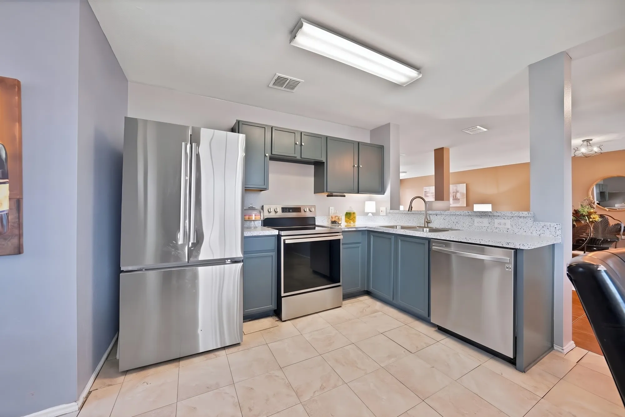 Kitchen with stainless steel appliances, light-toned tile flooring, blue cabinetry, and light-colored countertops