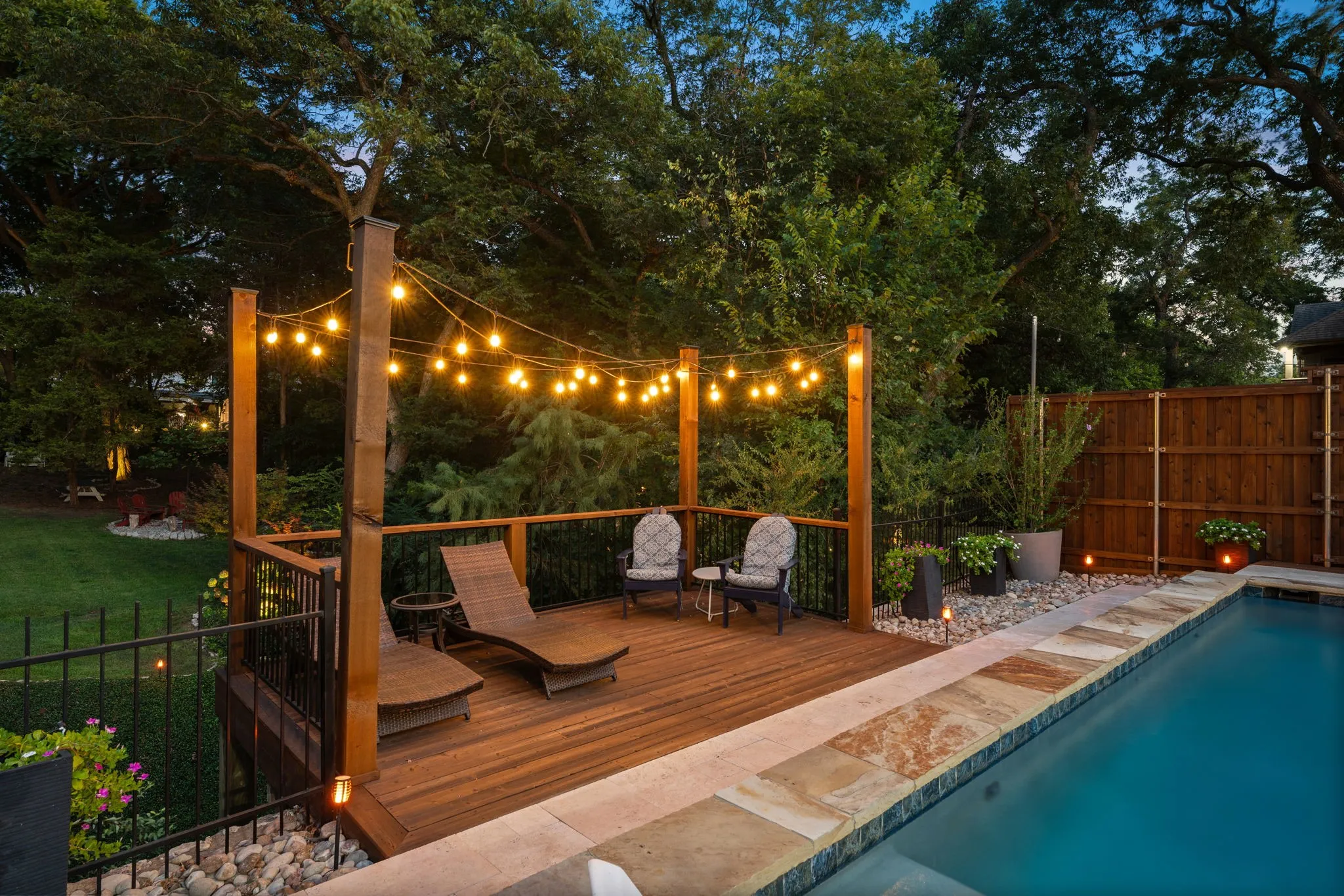 Hardwood deck with string lighting, adjacent to a swimming pool with natural stone coping