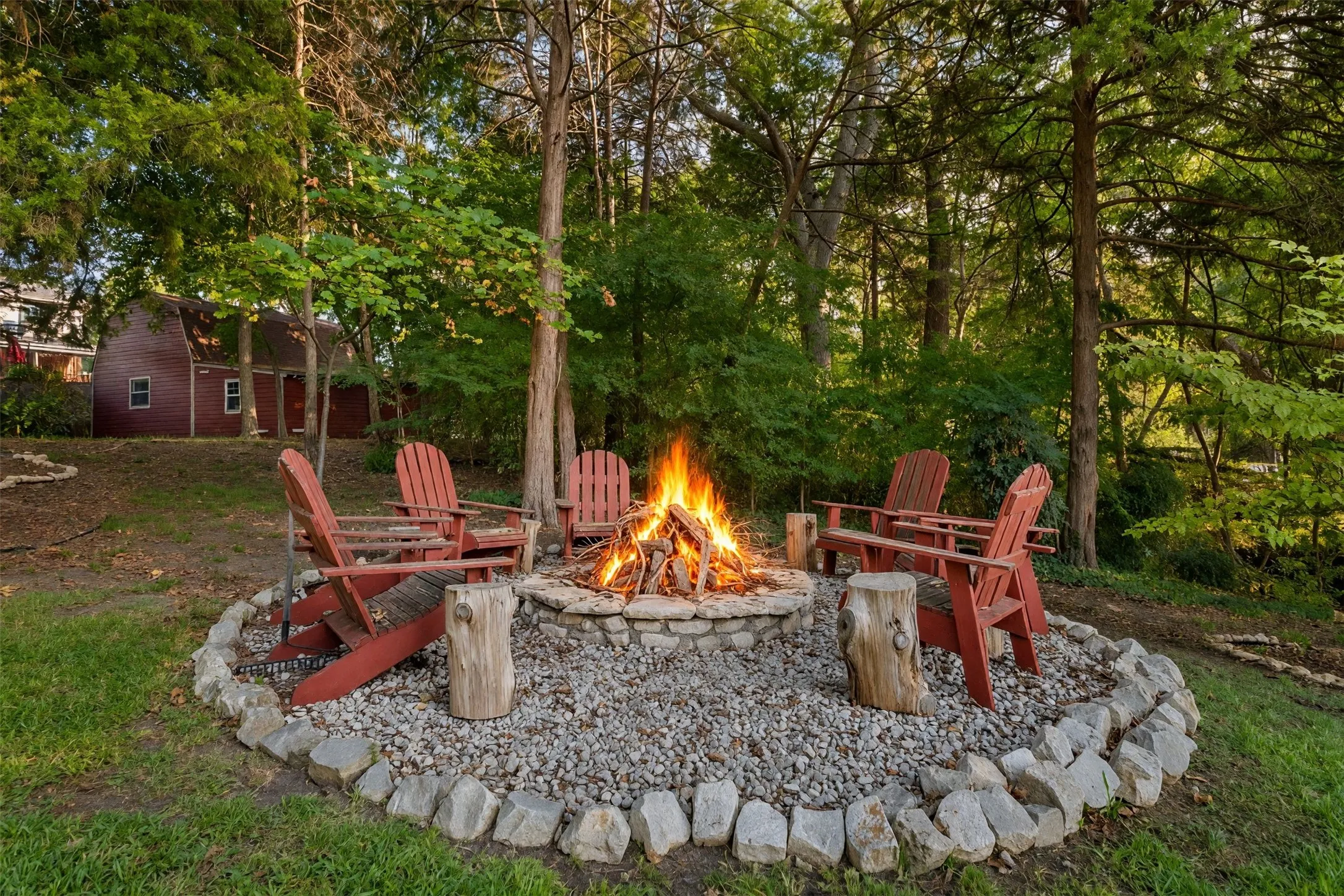 Stone-bordered fire pit with gravel ground cover, surrounded by mature trees
