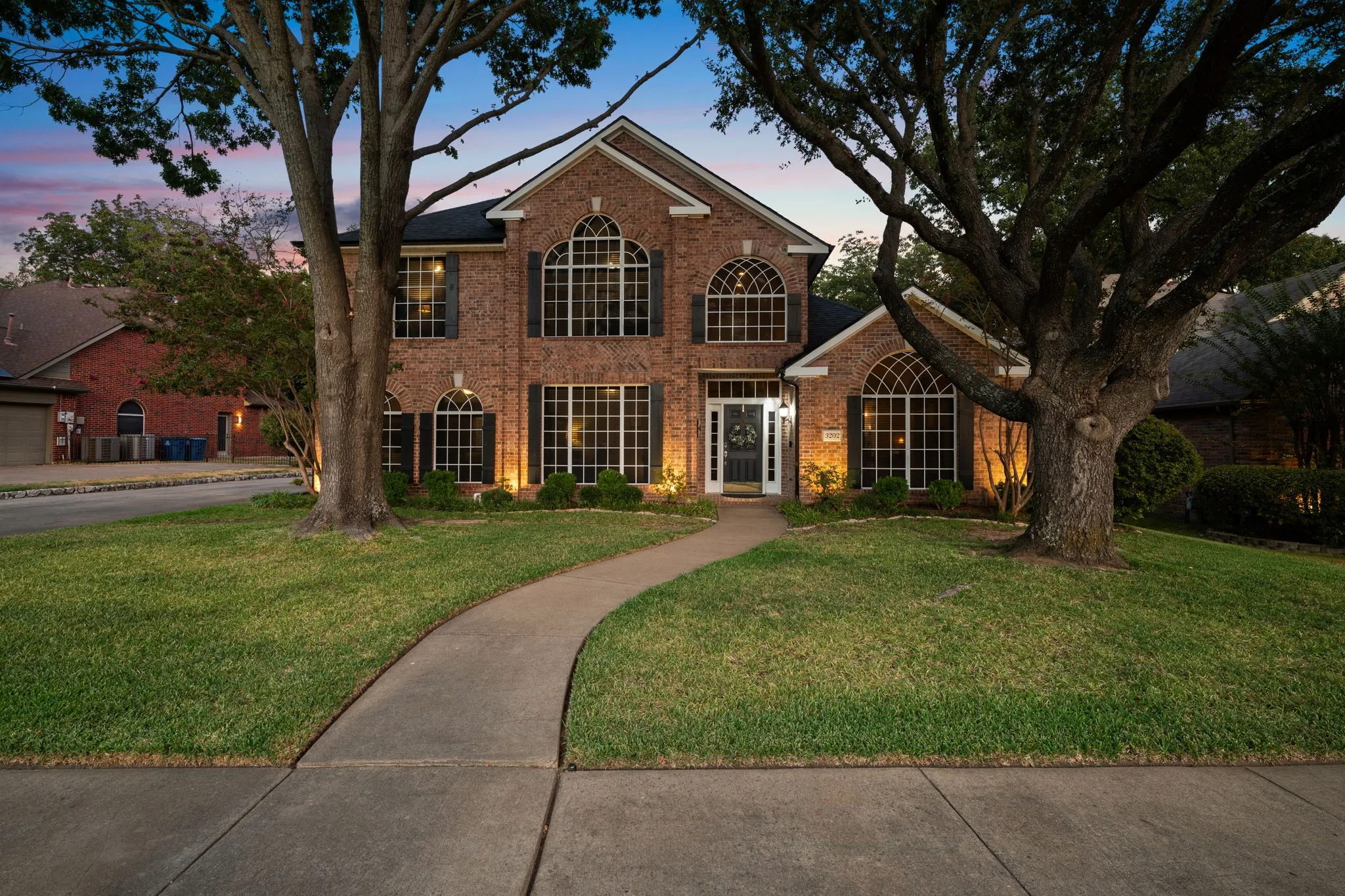 Brick facade residence with arched windows, custom shutters, and a prominent front entrance