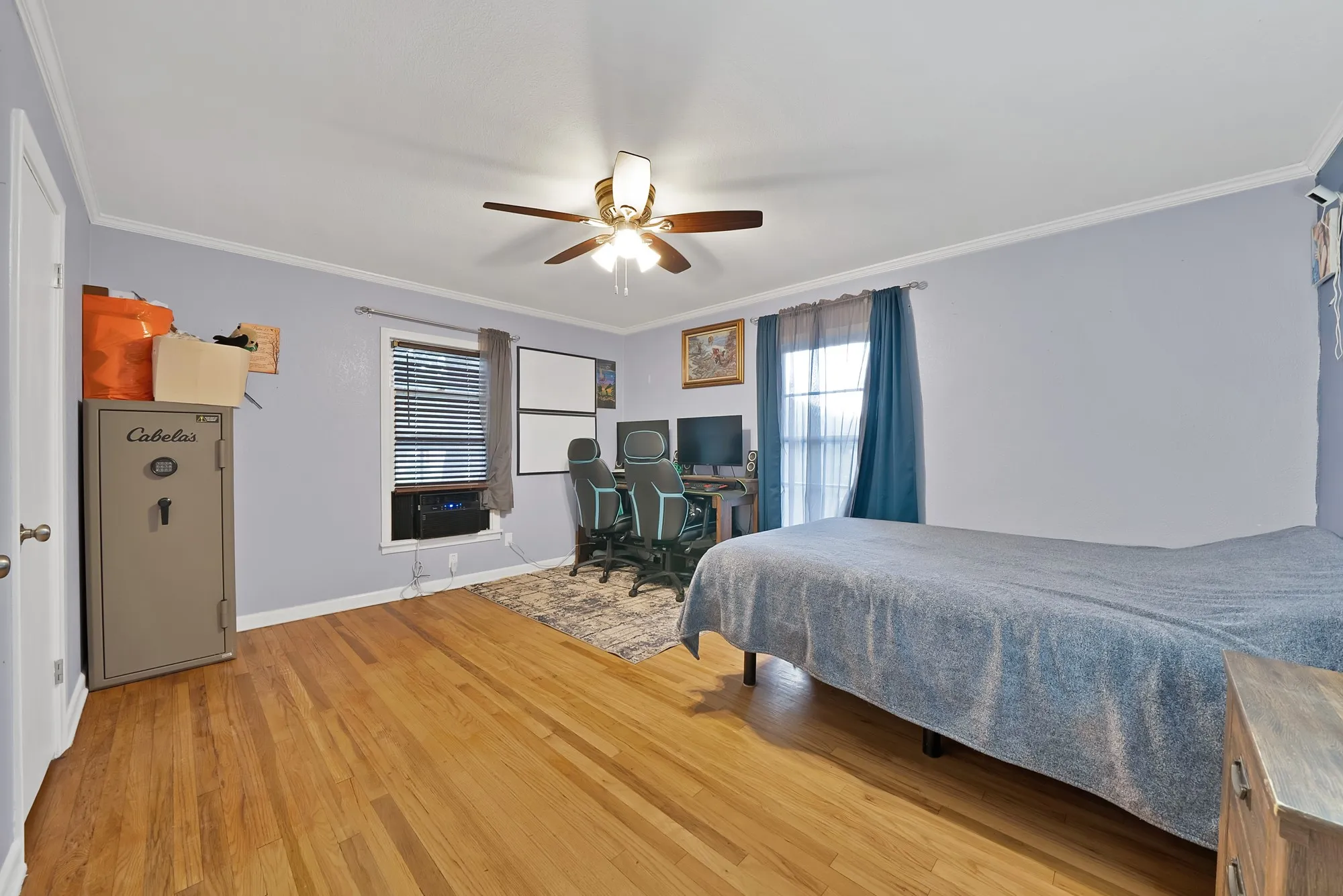 Wood-finish flooring, ceiling fan with integrated lighting, a window with blinds, and a secondary window with drapery