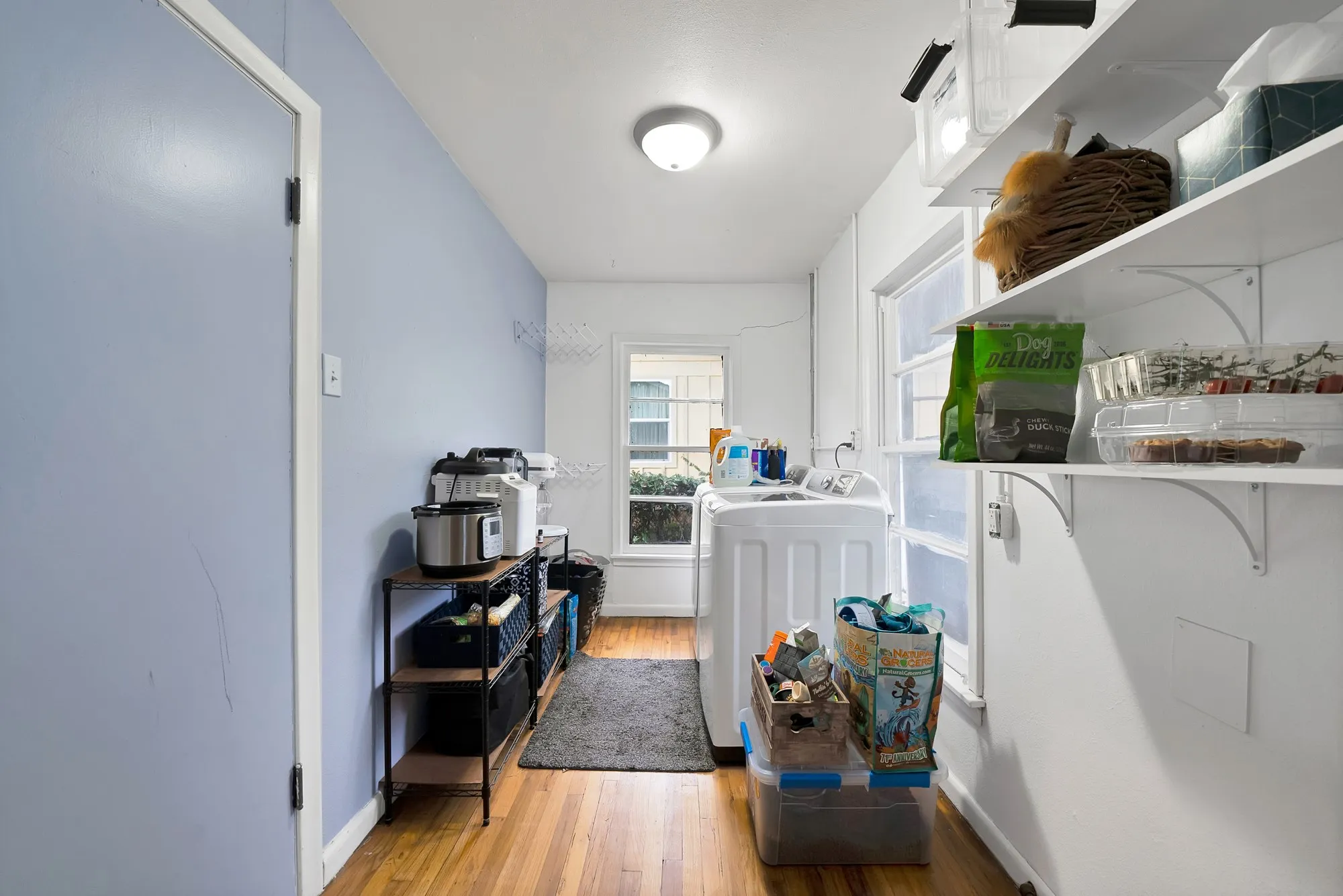 Laundry area featuring wood-finish flooring, multiple windows, and extensive wall-mounted shelving